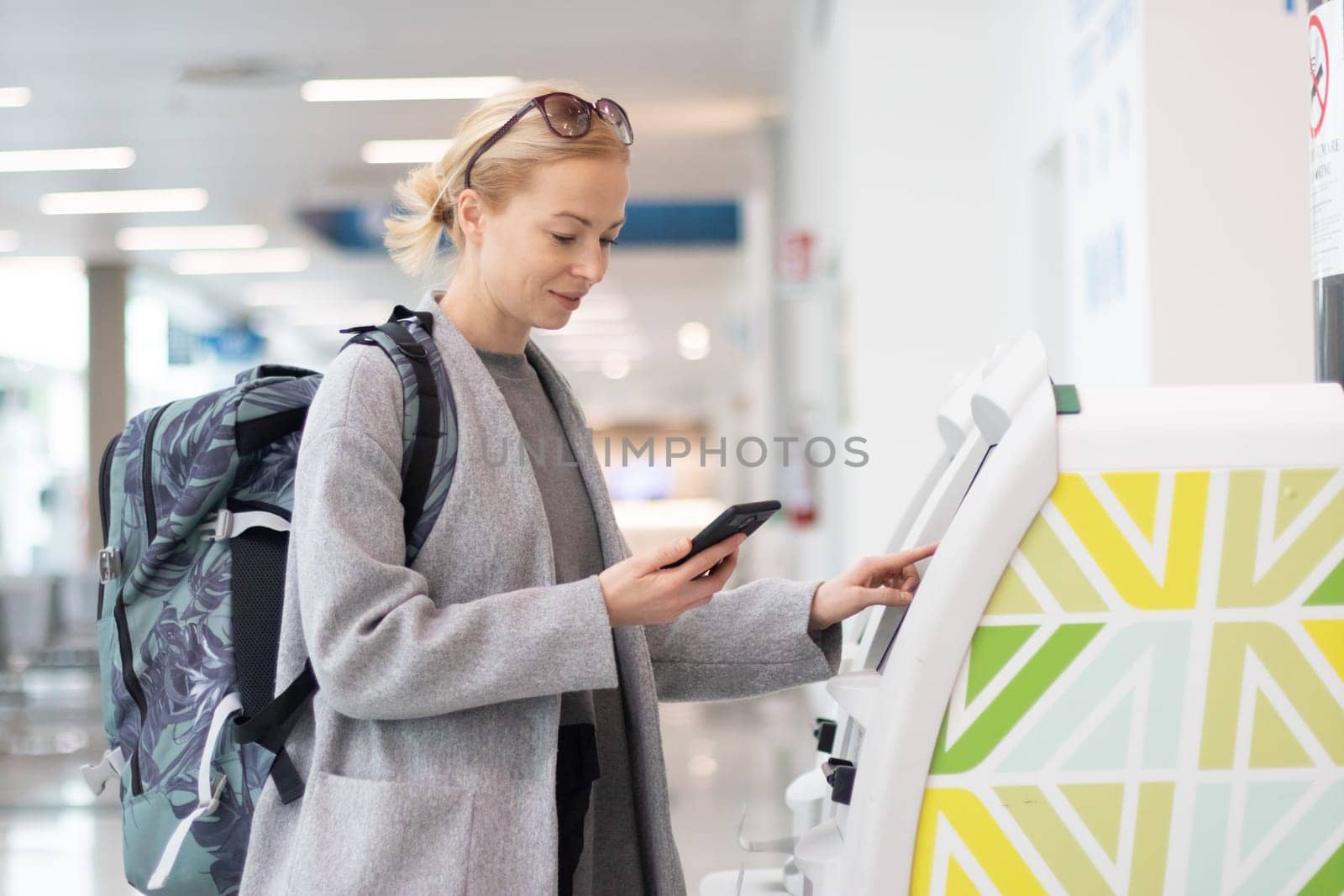 Casual caucasian woman using smart phone application and check-in machine at the airport getting the boarding pass. Modern technology on airport.