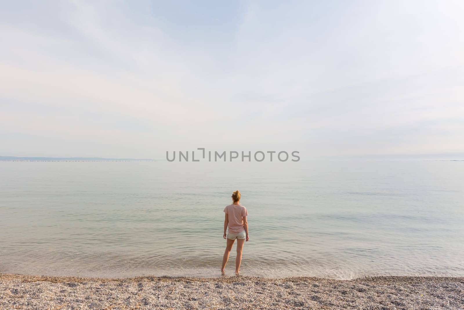 Happy Carefree Woman Enjoying Late Afternoon Walk on White Pabbled Beach in Summer.