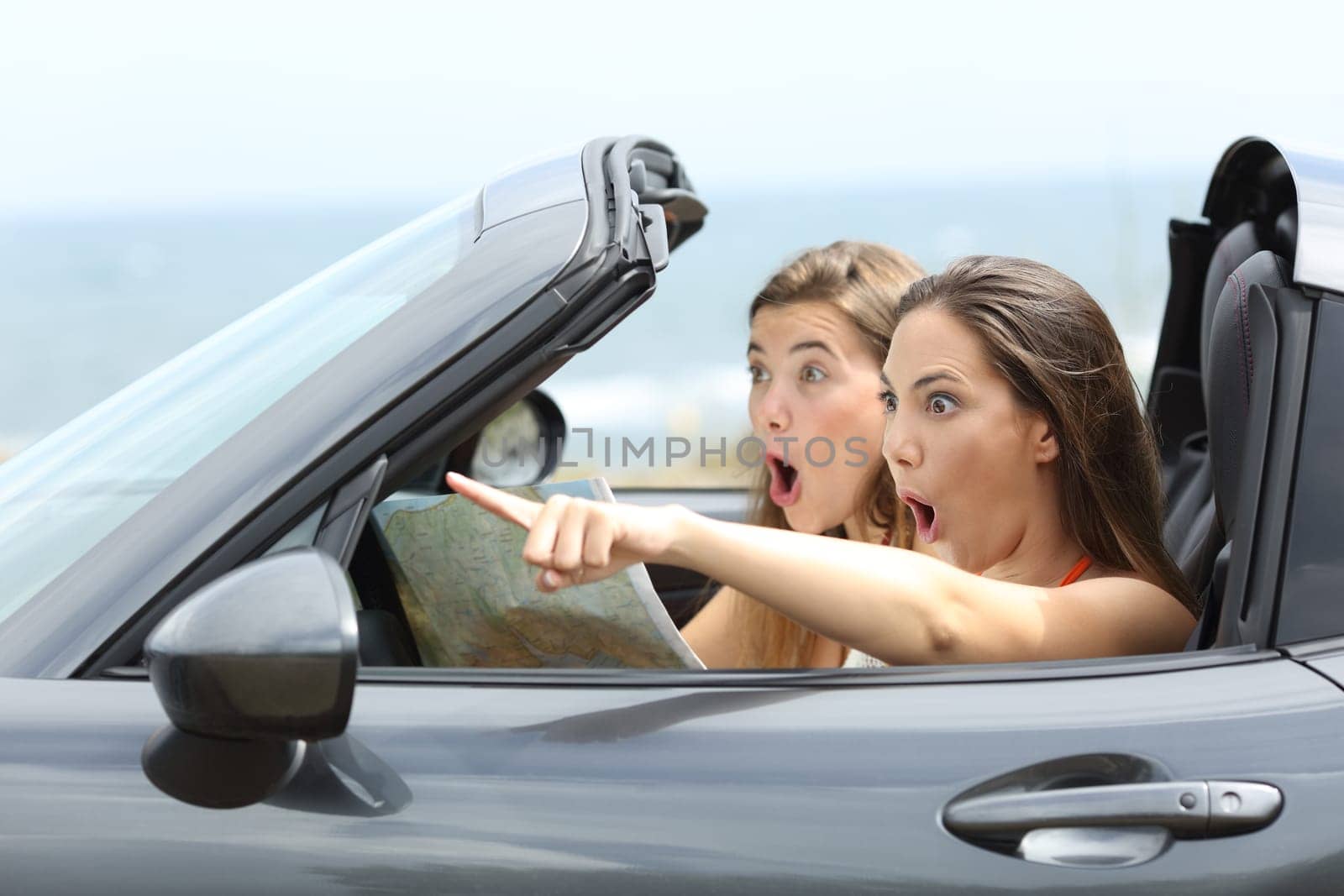 Amazed girls in a car pointing away on summer vacations