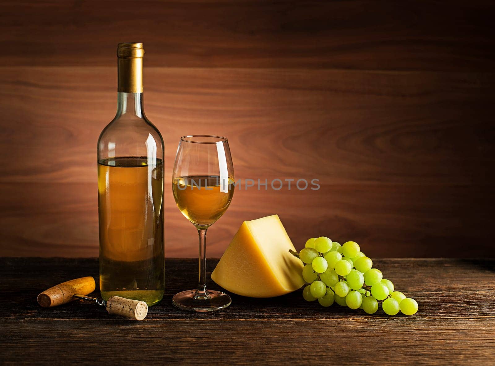 Bottle of white wine with snack food on old board. Glass of wine and cork with wooden background.