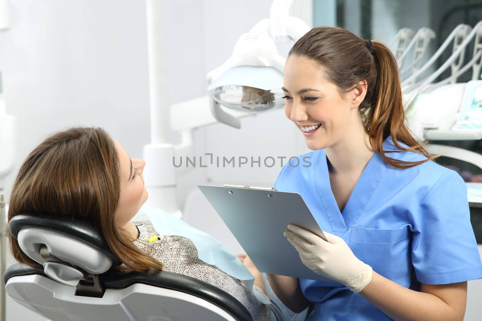 Dentist holding a medical history asking information to a patient before treatment sitting on a chair in a clinic box