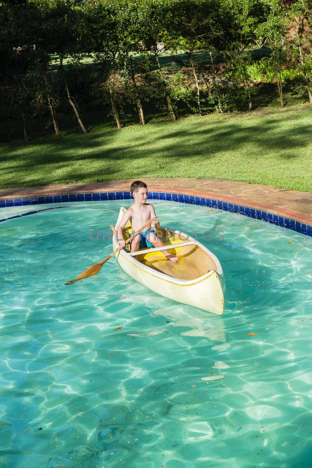 Boy swimming pool water with kayak canoe paddle playing childhood.
