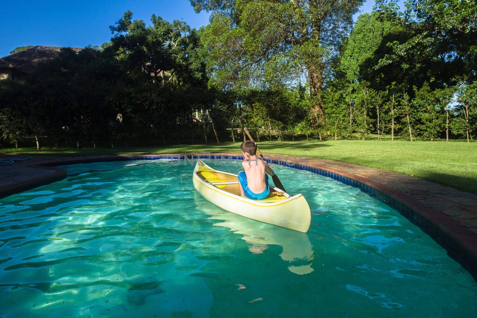 Boy swimming pool water with kayak canoe paddle playing childhood.