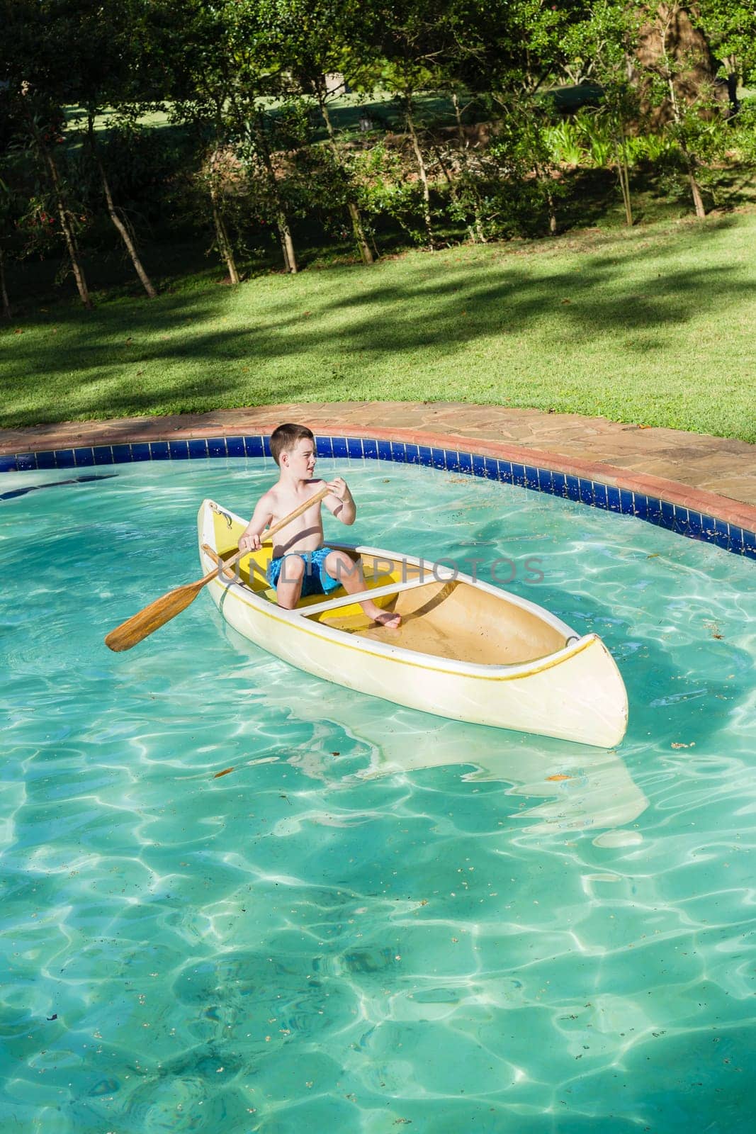 Boy swimming pool water with kayak canoe paddle playing childhood.