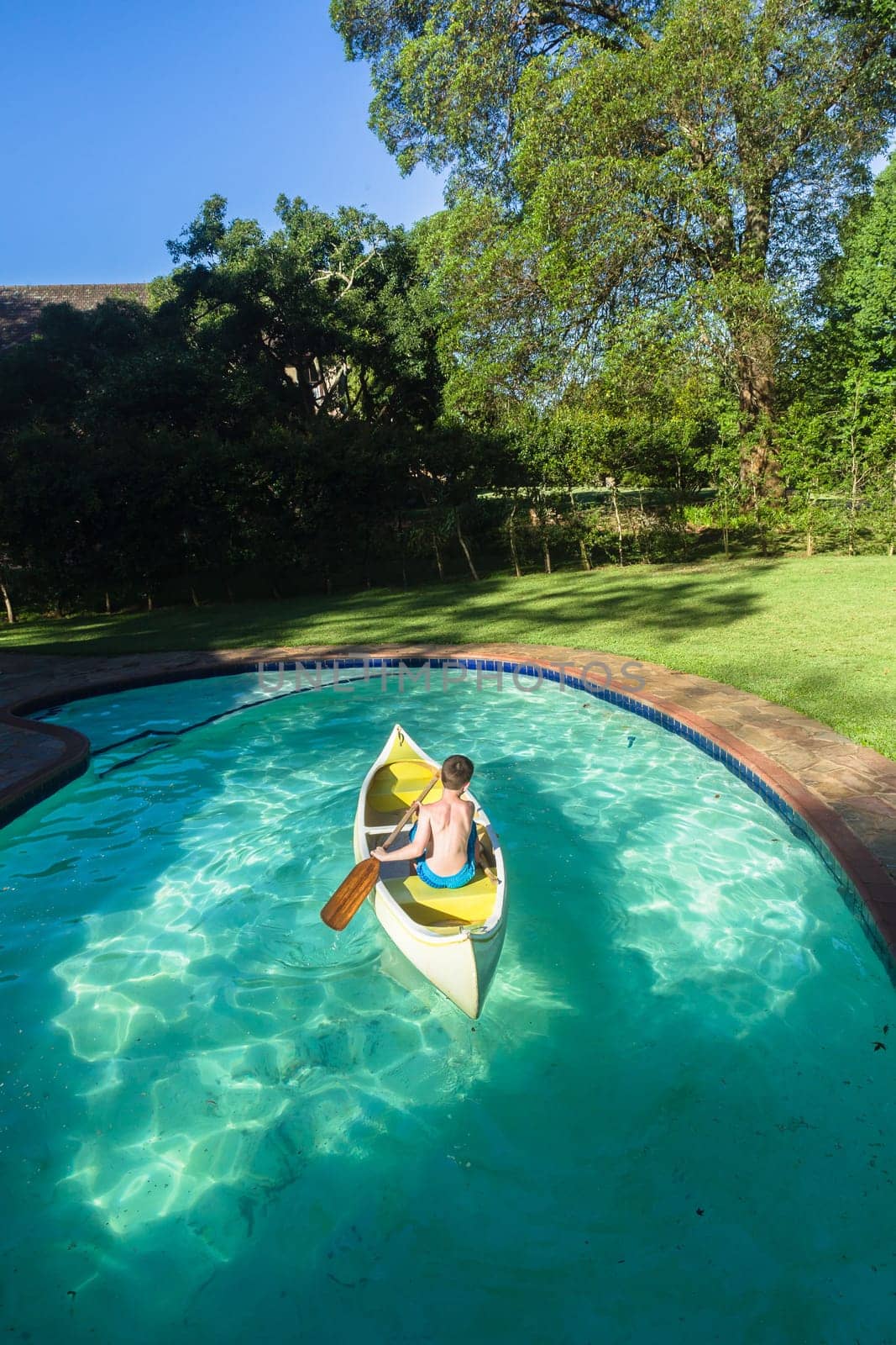 Boy swimming pool water with kayak canoe paddle playing childhood.