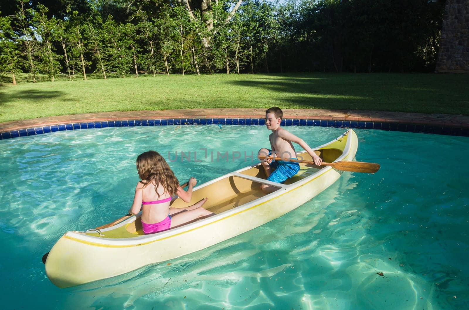 Children boy girl summer playtime in swimming pool waters with  kayak canoe paddles