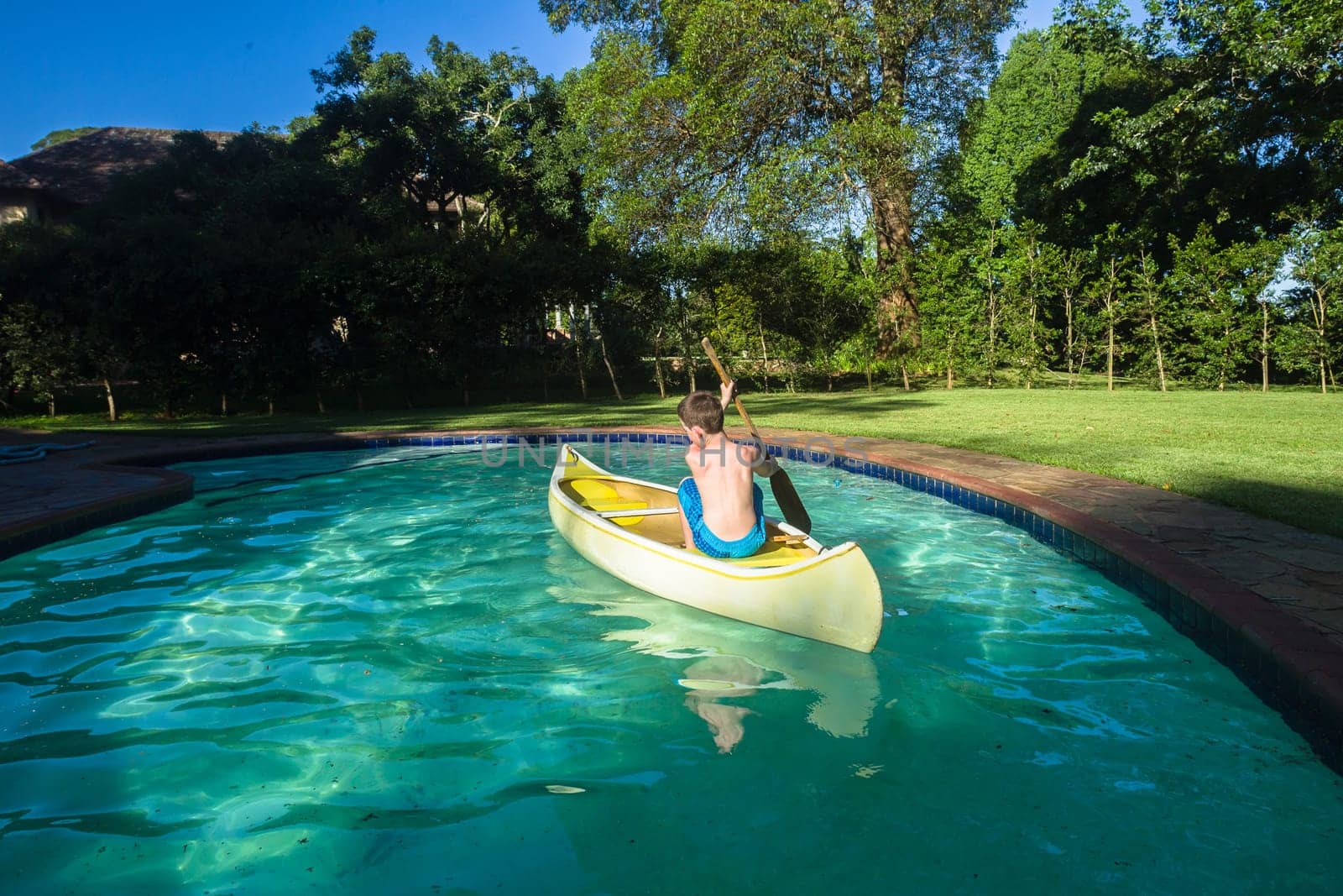 Boy swimming pool water with kayak canoe paddle playing childhood.