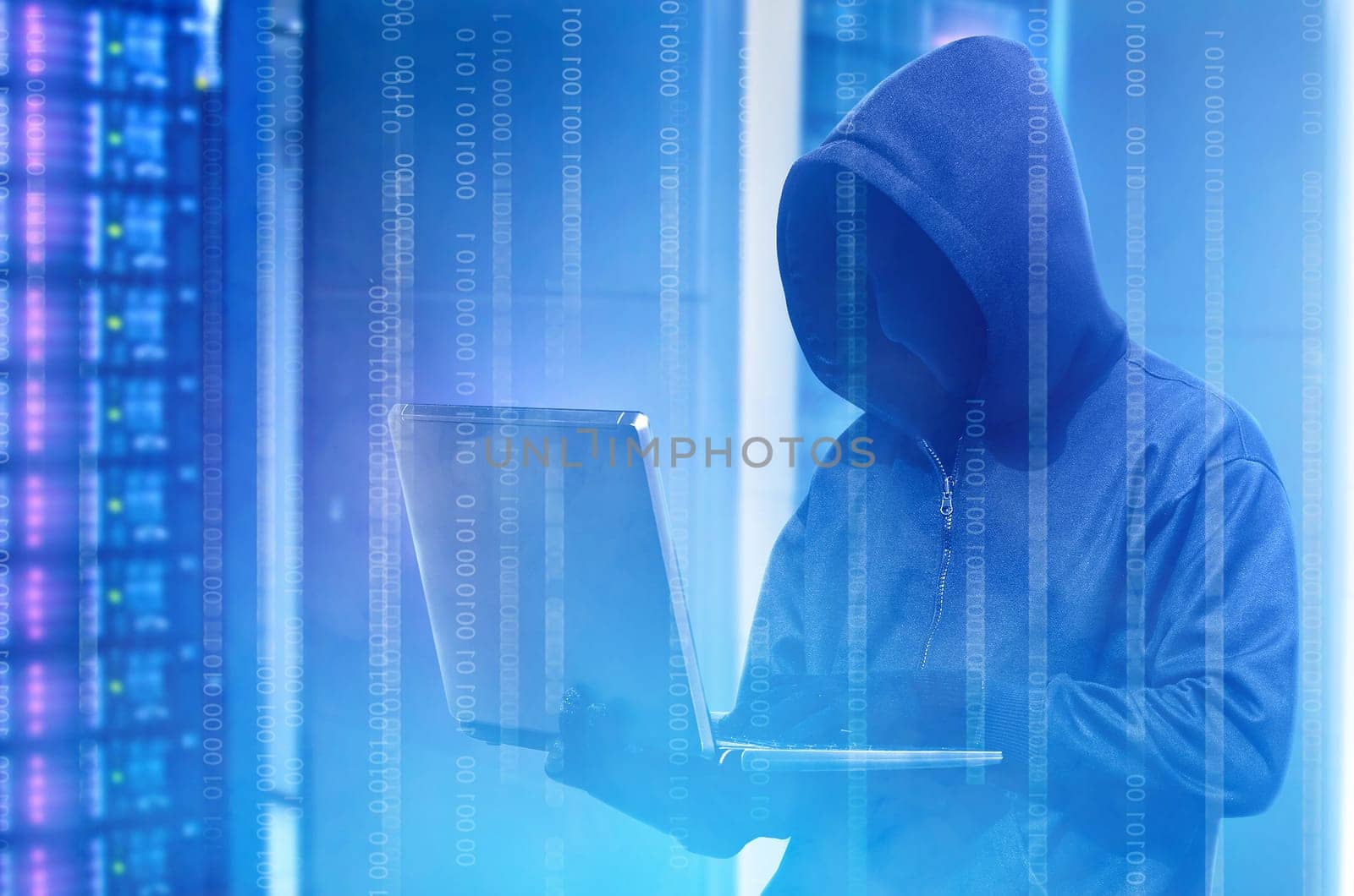 Hacker in black hoodie holding laptop with binary code on virtual screen with modern storage of server in the data center on the background