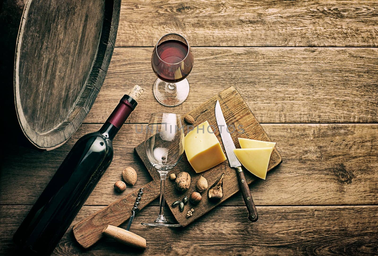 Bottle of red wine with glasses and cheese on wooden and barrel rustic background.