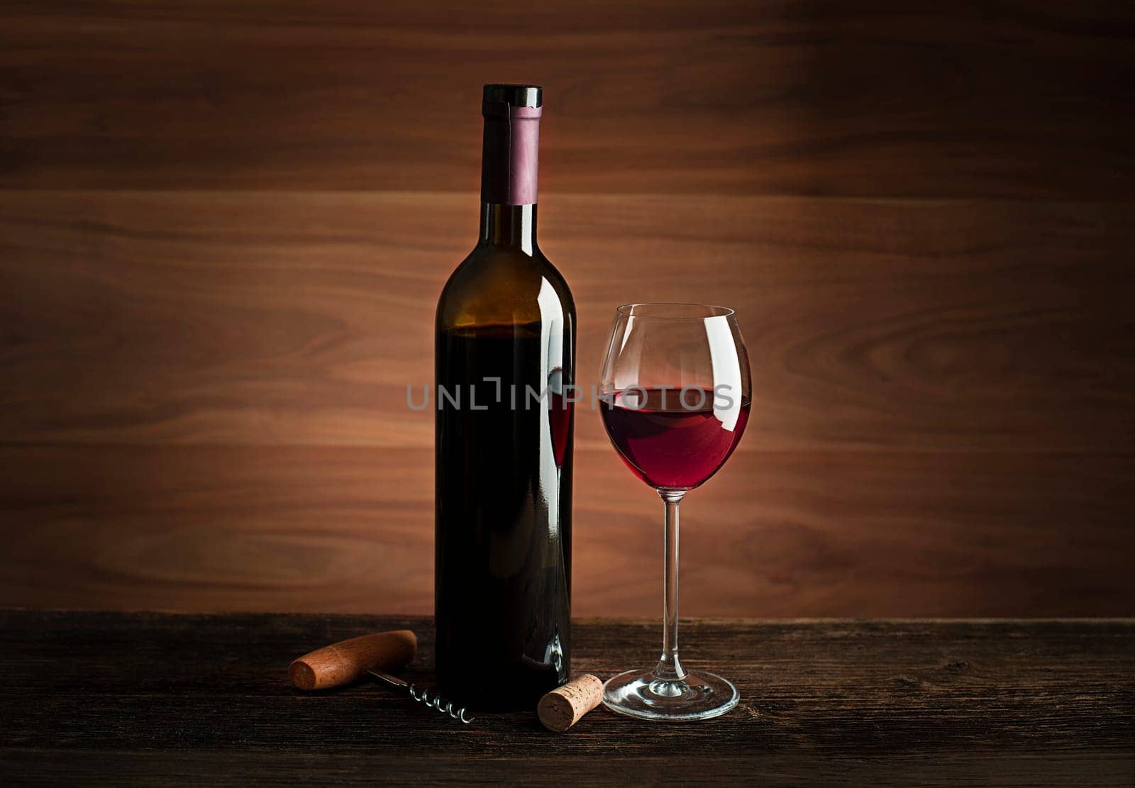 Glass and bottle of red wine on wooden background.