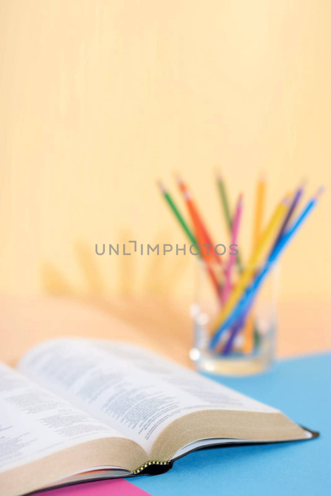 Bible book (blured text) and glass with a set of colored pencils on a colored paper background ready to be studied and underlined. Ready for Bible study.