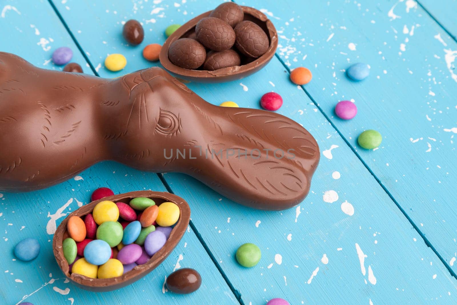 Delicious chocolate Easter bunny, eggs and sweets on rustic background