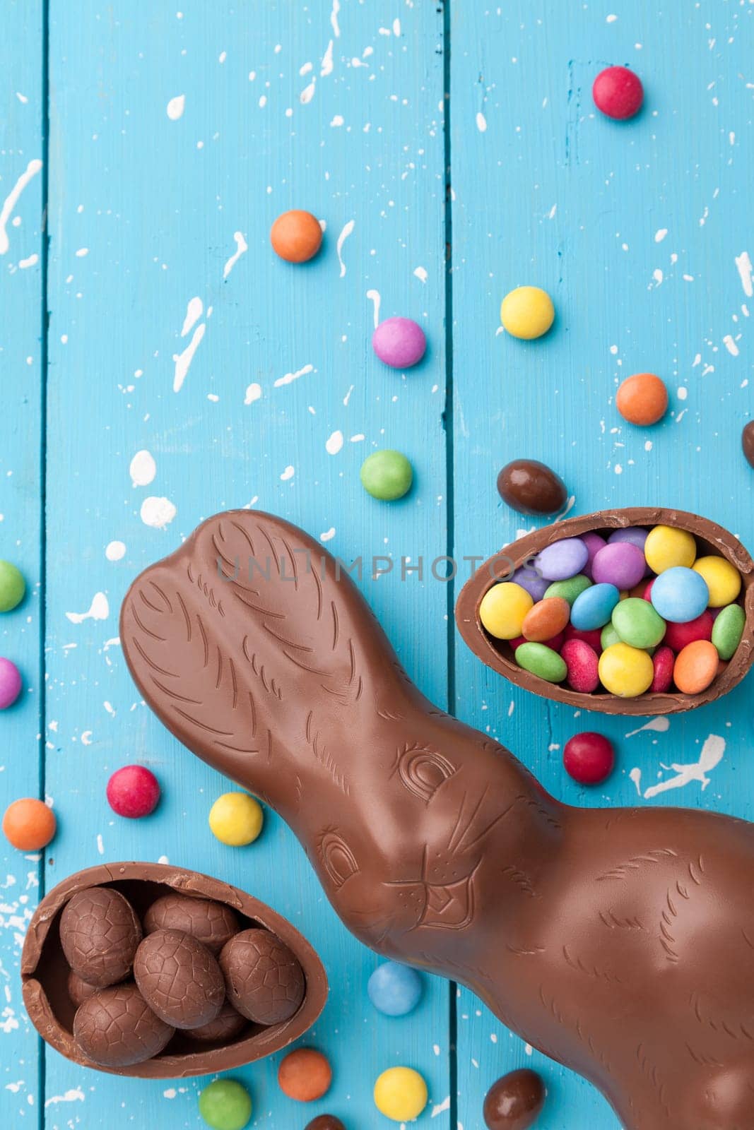 Delicious chocolate Easter bunny, eggs and sweets on rustic background