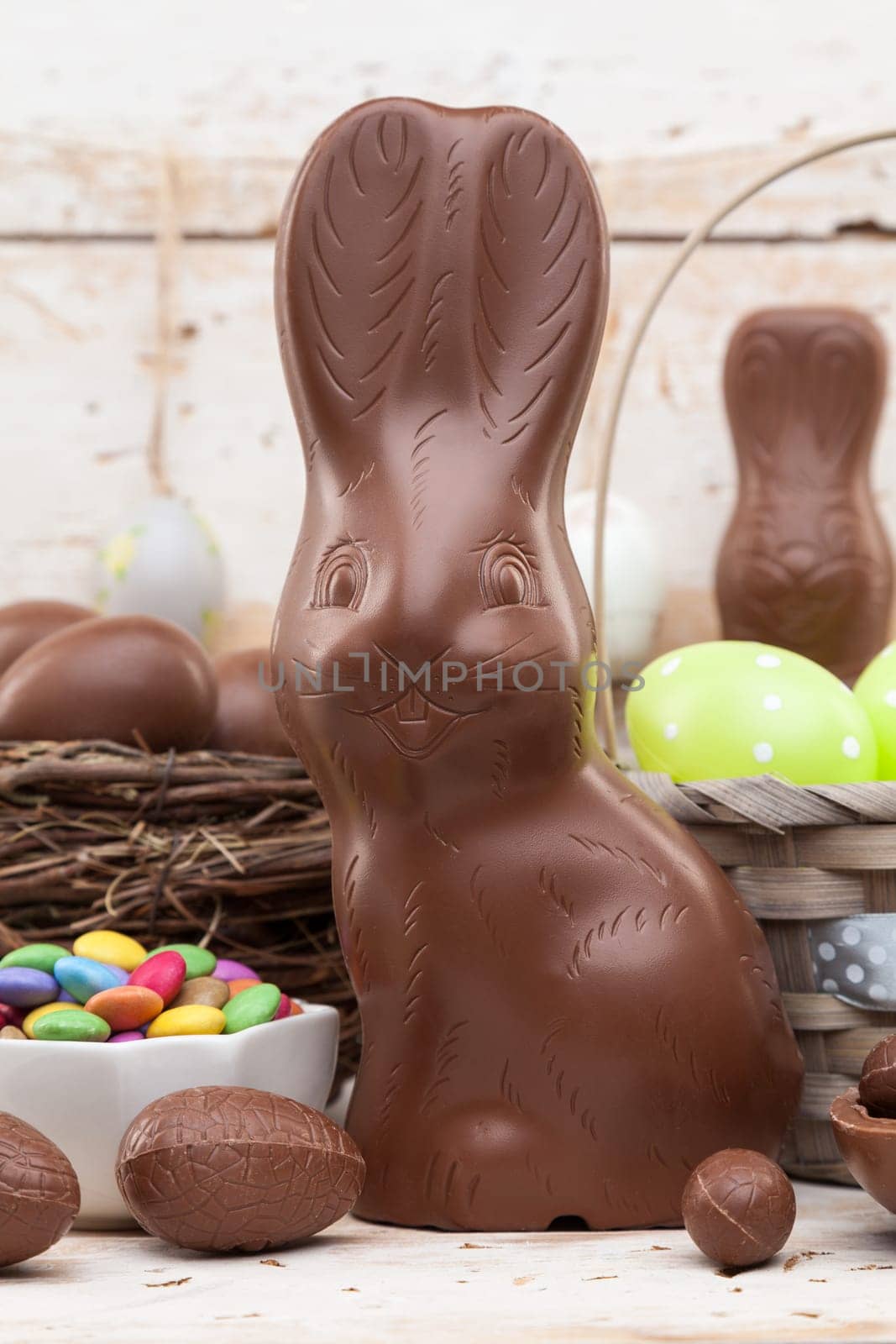 Delicious chocolate Easter bunny, eggs and sweets on rustic background