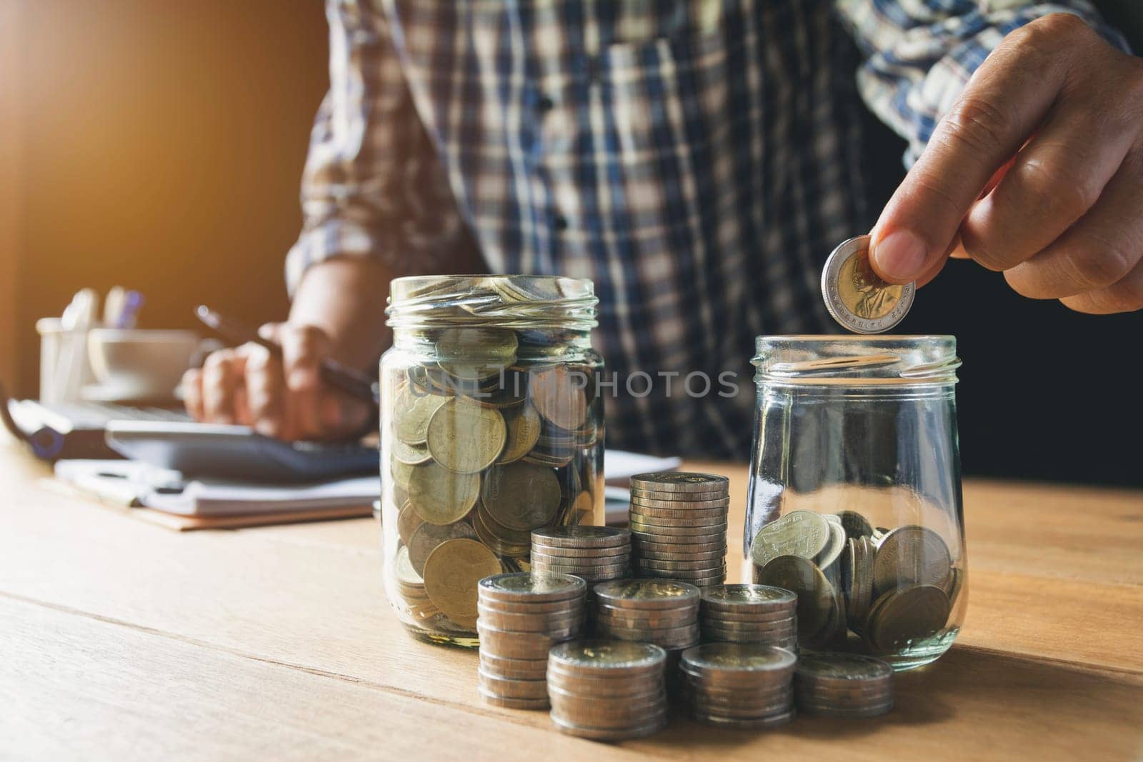 Hand putting money coin in the glass jar. Saving money, financial and accounting concept.
