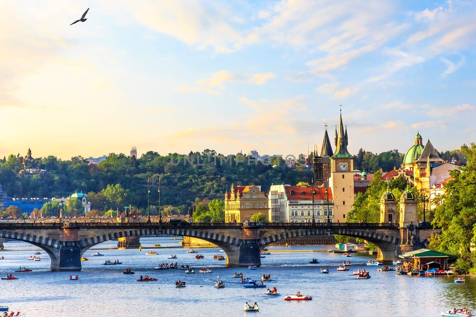 The Vltava River in Prague with people floating on paddleboats near Manes Bridge.