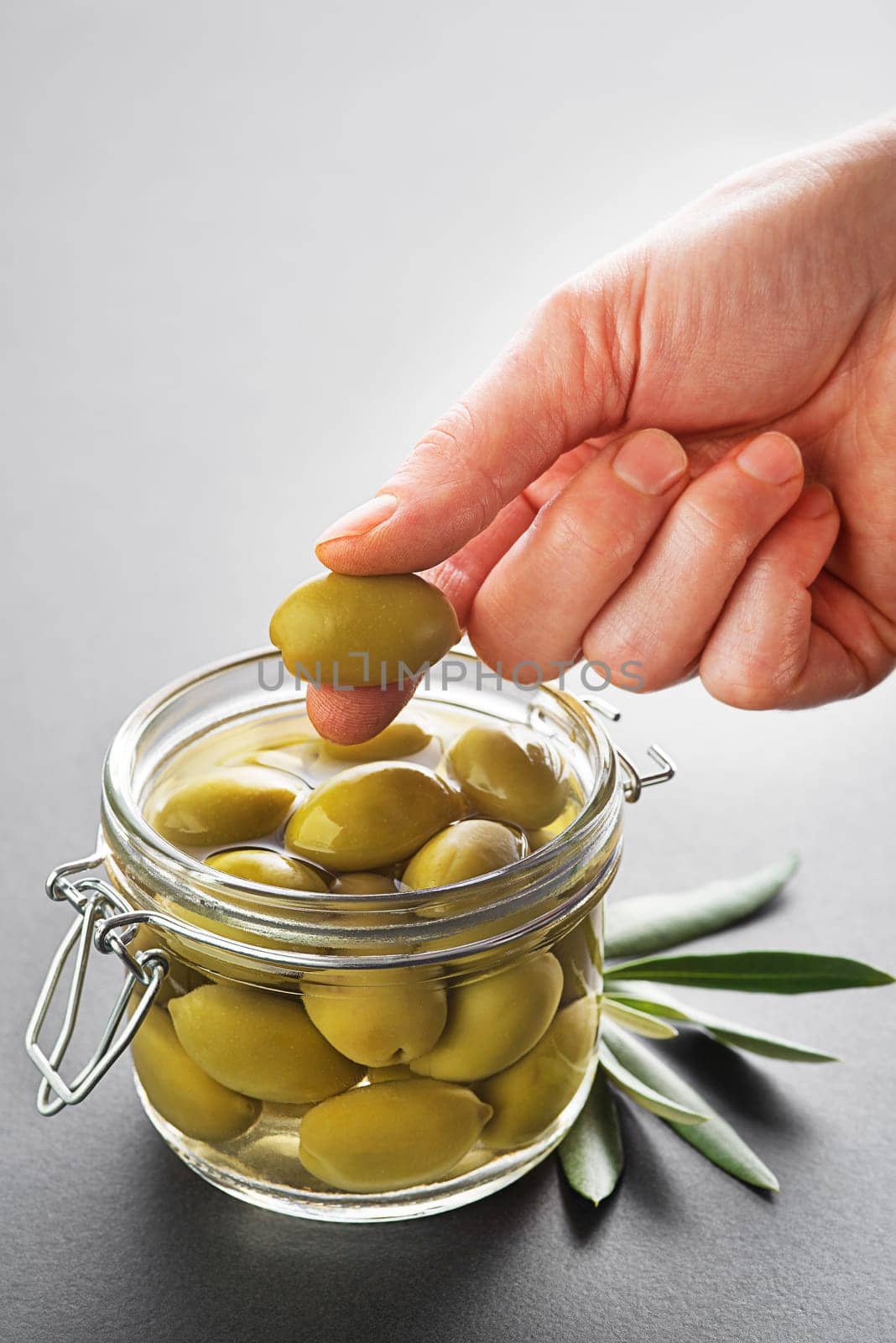 Pickled green olives in glass jar close up. Eating with hands.