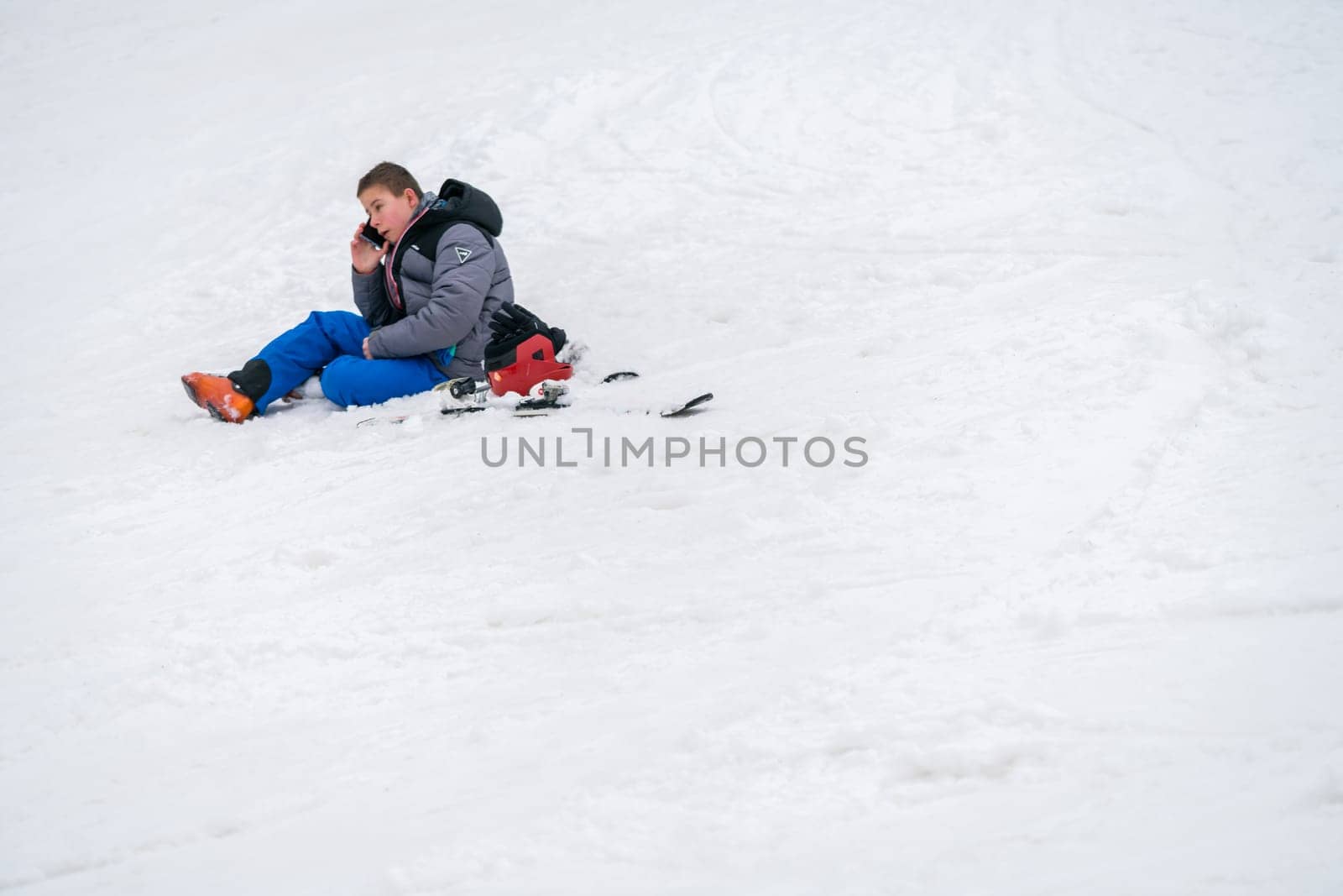 Szklarska Poreba, Poland - February 2019 : Young boy calling for help on his mobile phone after skiing or snowboarding accident on the mountain slope, Szrenica mountain, Karkonosze