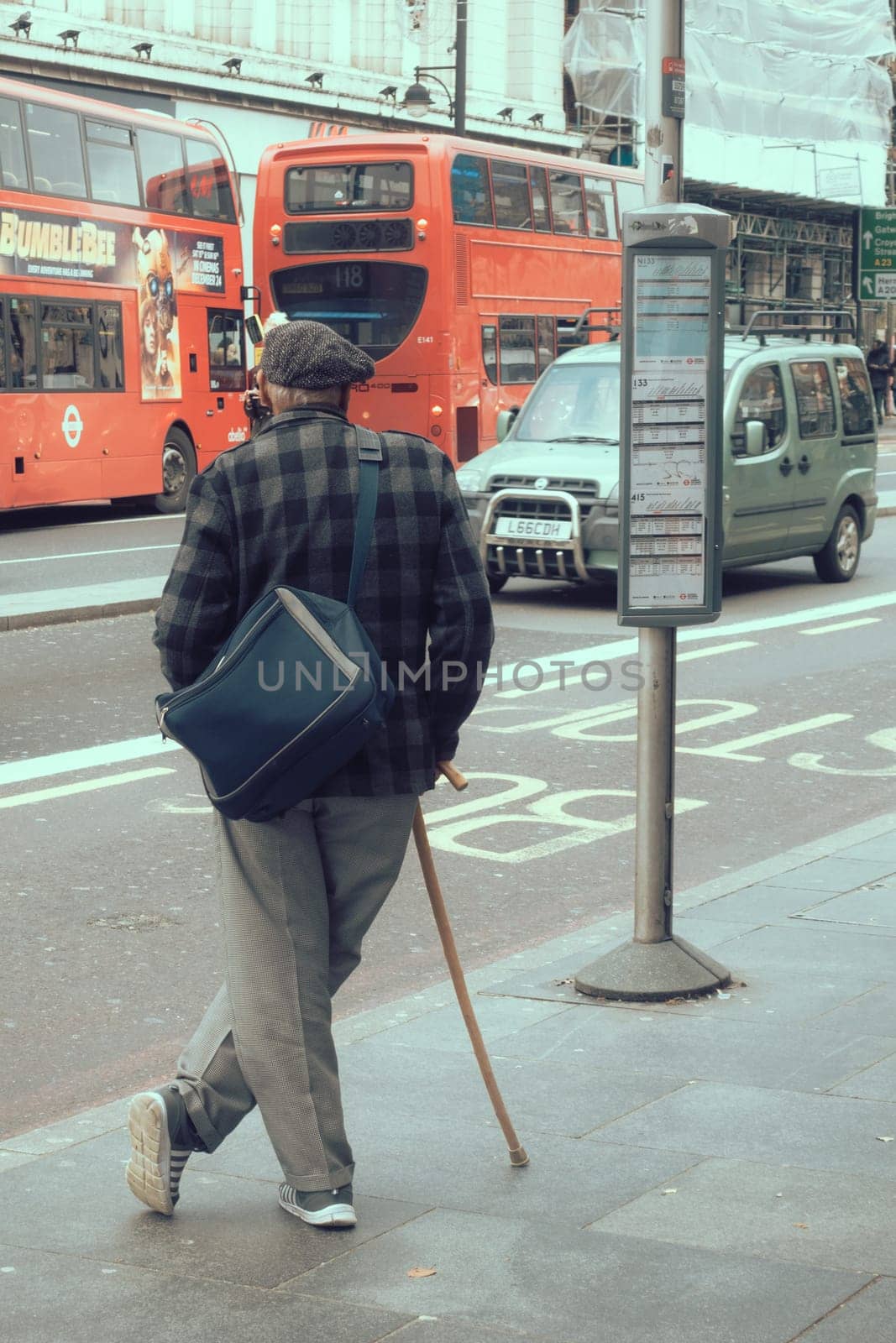 London, England - December 2018 : Elderly men with a walking stick waiting for bus on the bus stop in Brixton