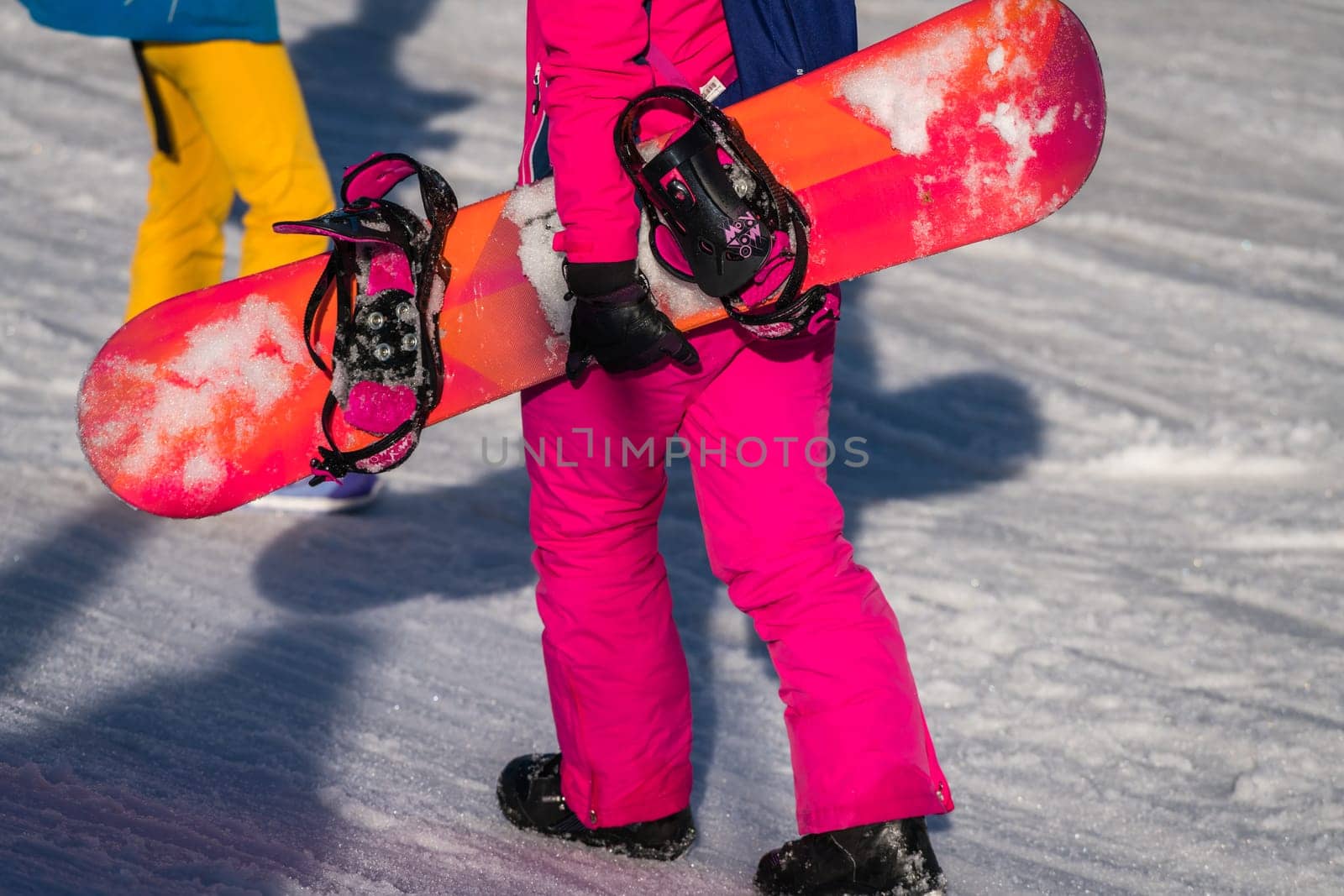 Szklarska Poreba, Poland - February 2019 : Snowboarder dressed in pink ski jacket walking up the slope carrying her snowboard