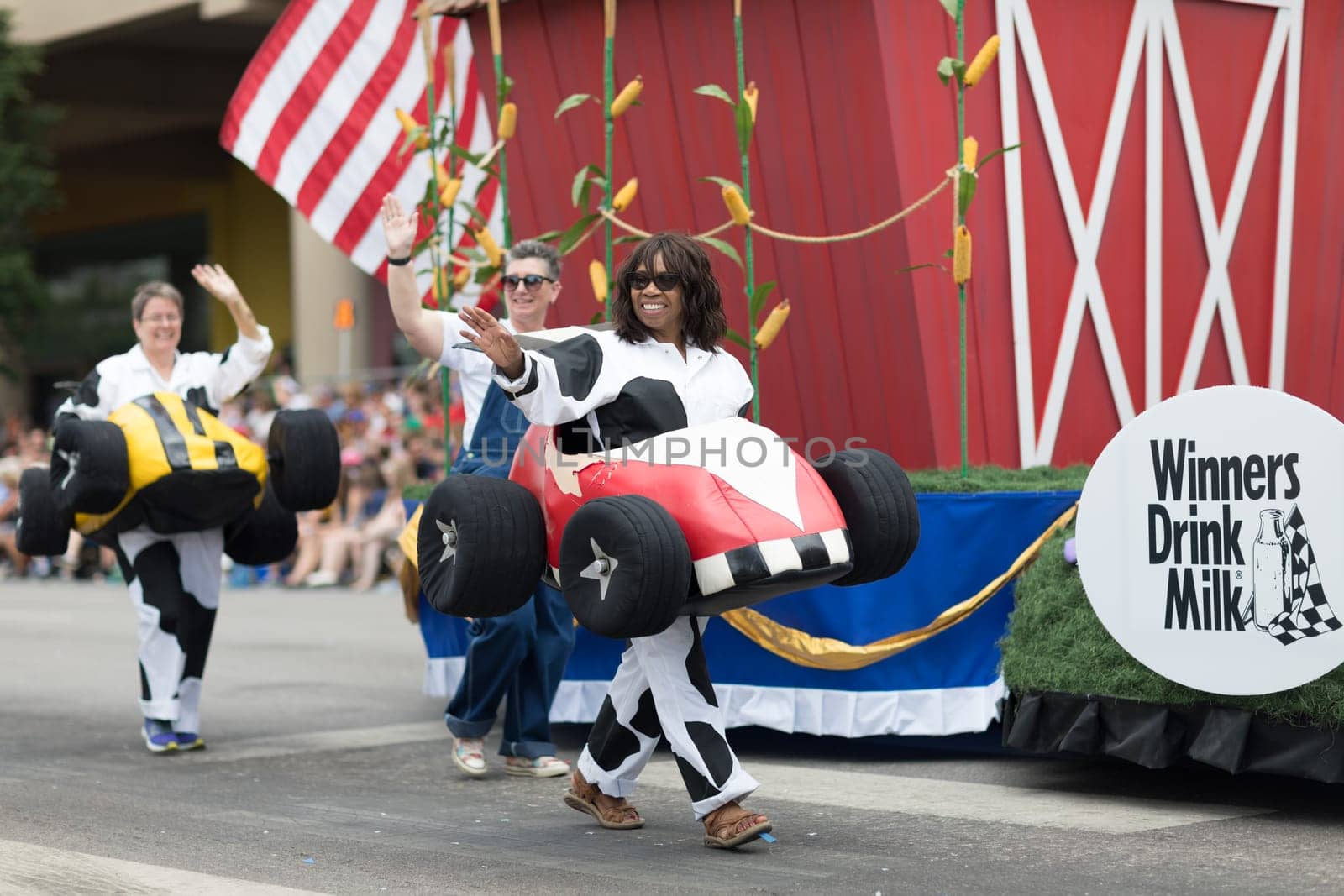 Indianapolis, Indiana, USA - May 26, 2018,  People with race car outfits walking along a float with a giant cow, promoting milk drinking, at the Indy 500 Parade