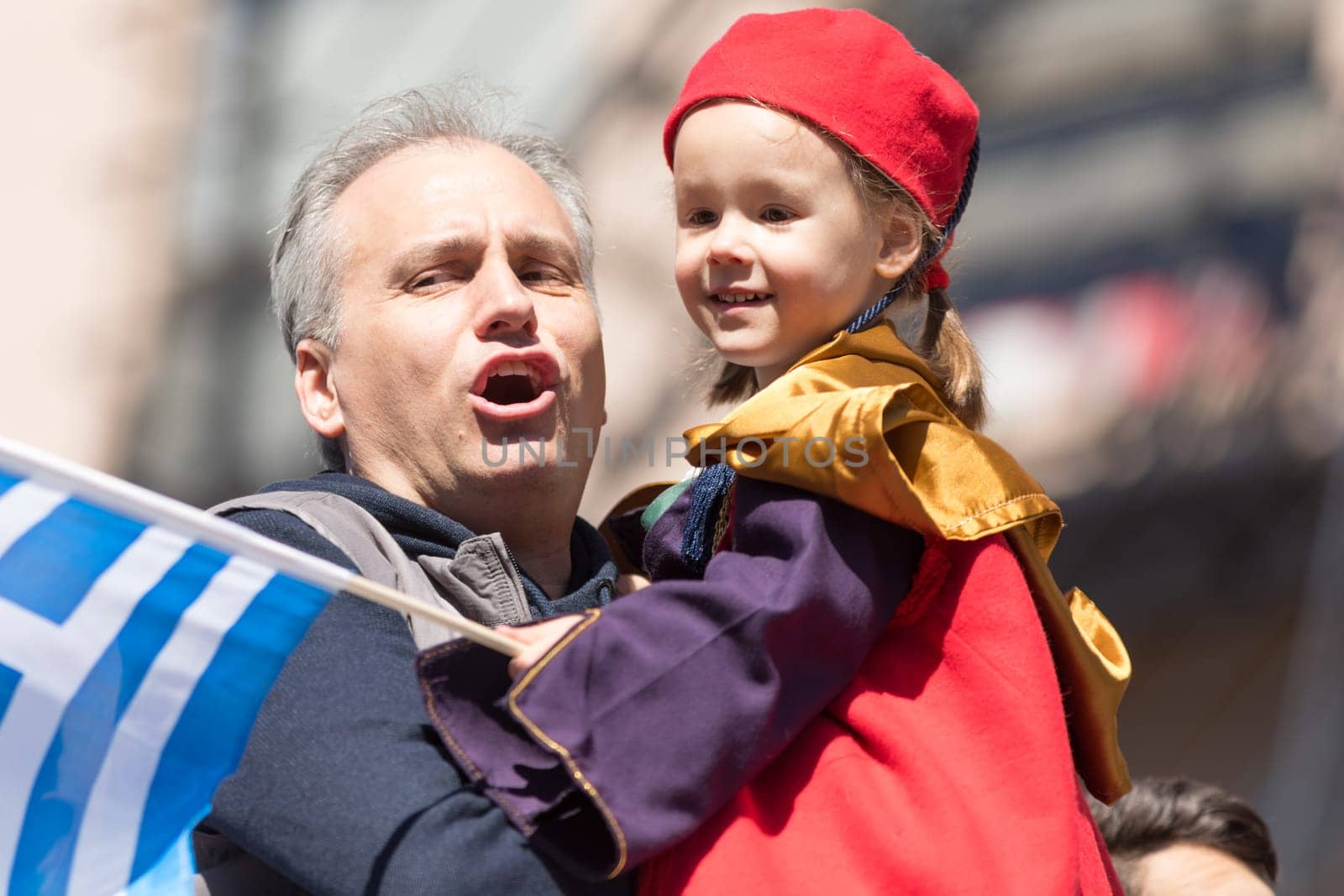Chicago, Illinois, USA - April 29, 2018 Greek man hold his child wearing traditional clothing while the child waves the greek flag at the Greek Independence  Day Parade