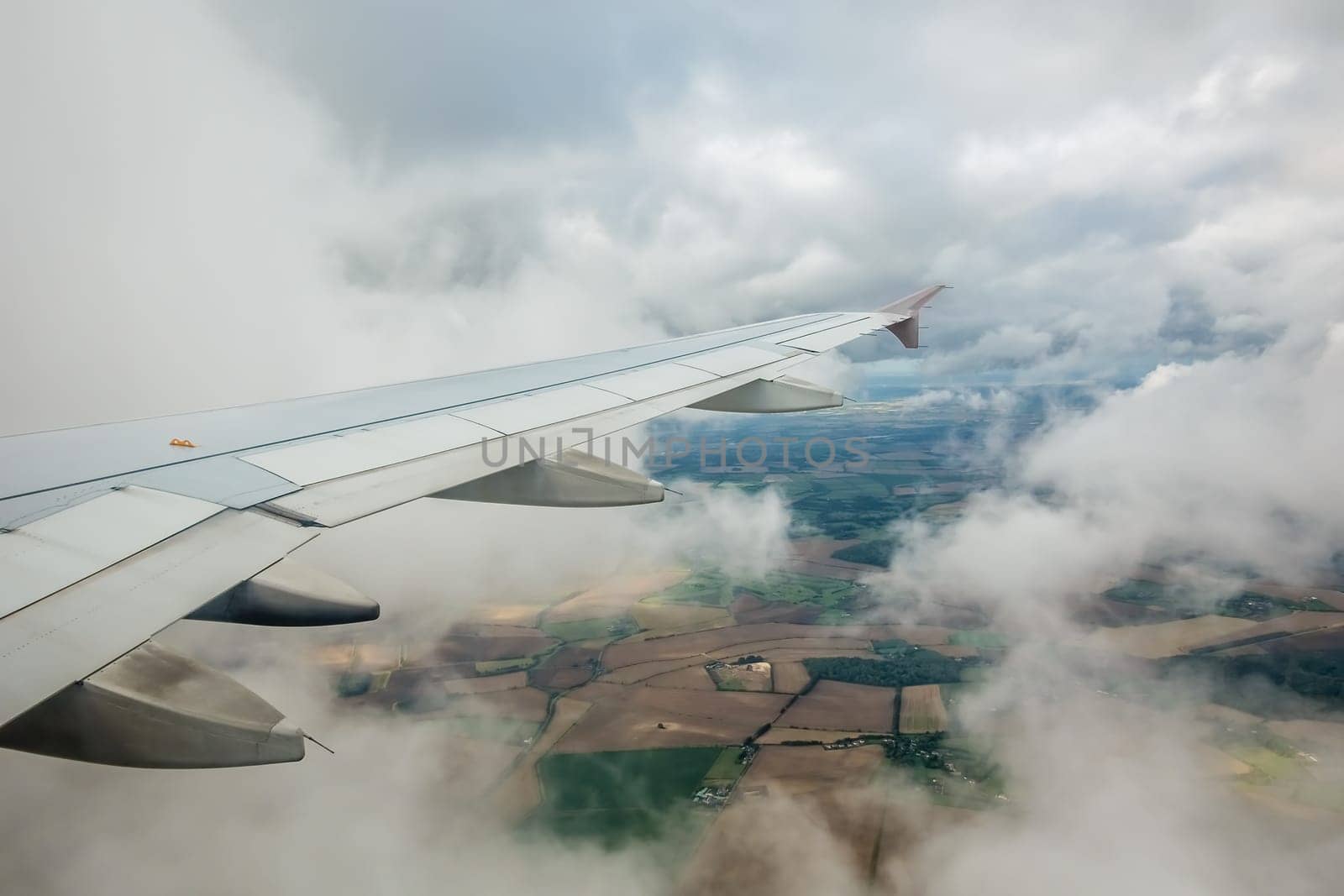 Window view of the wing of an airplane flying above the clouds and english countryside