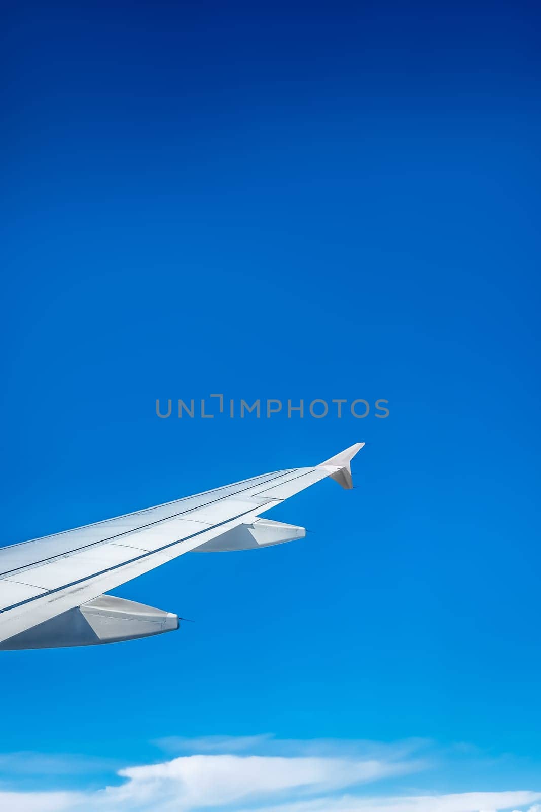 Window view of the wing of an airplane flying above the clouds