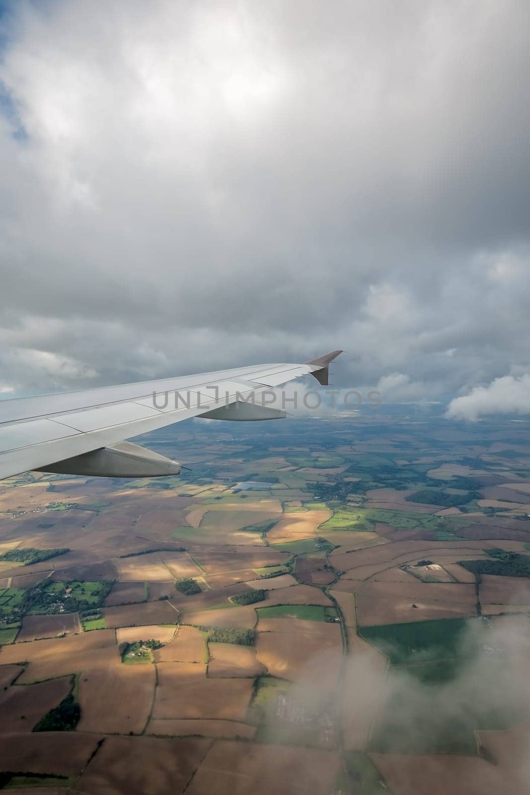 Window view of the wing of an airplane flying above the clouds and english countryside