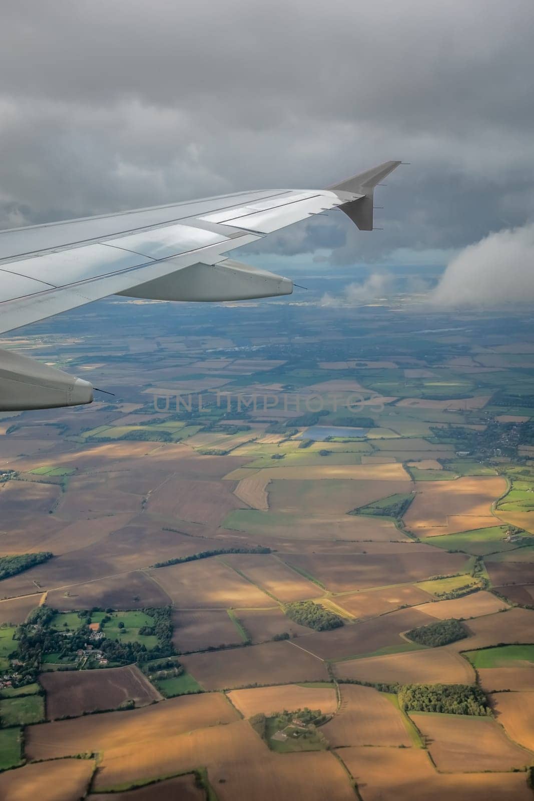 Window view of the wing of an airplane flying above the clouds and english countryside