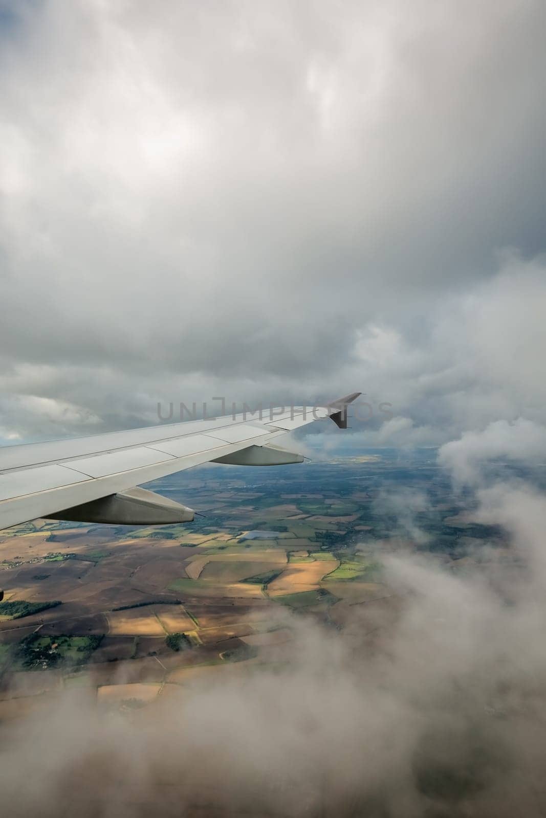 Window view of the wing of an airplane flying above the clouds and english countryside