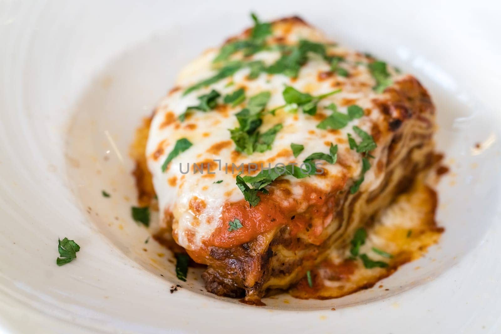 Portion of a delicious beef lasagne with melting cheddar, mozzarella and ricotta cheeses, garnished with parsley