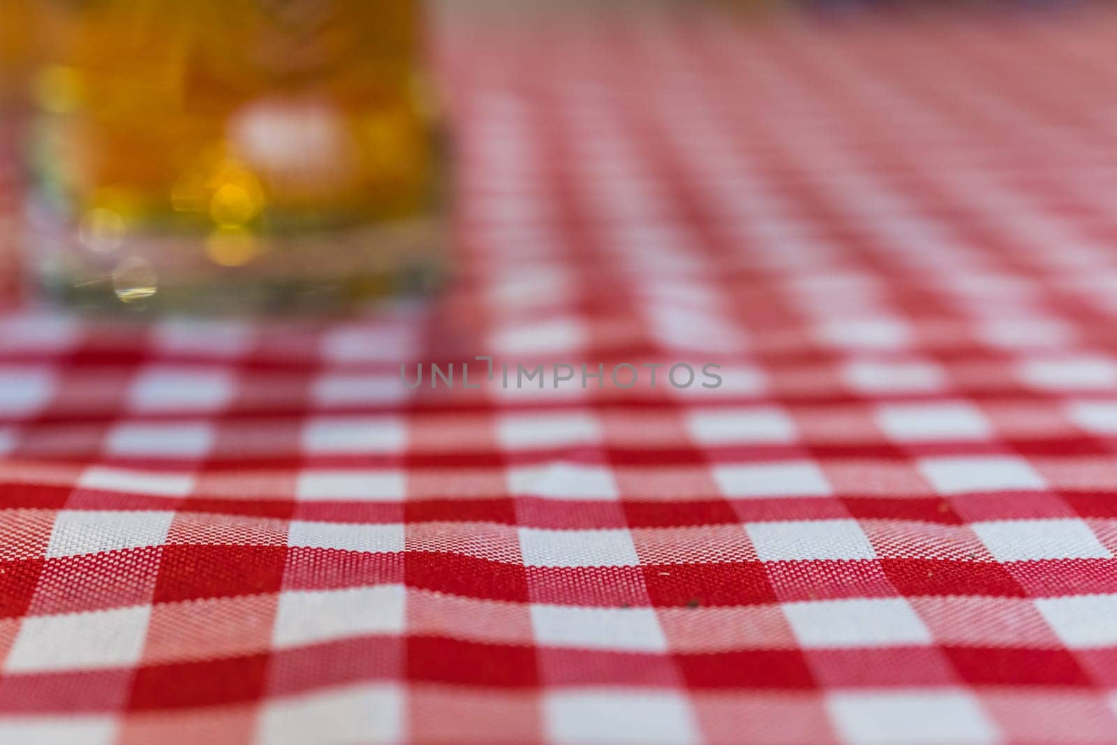 Abstract image of defocused glass of beer on a chequered tablecloth on a table in a restaurant