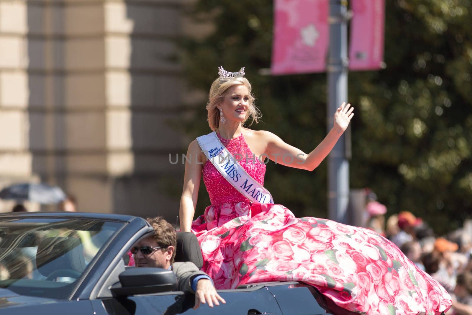 Washington, D.C., USA - April 14, 2018 Miss Maryland wearing a pink dress with pictures of cherry flowers on a car going down the road in the 2018 National Cherry Blossom Parade