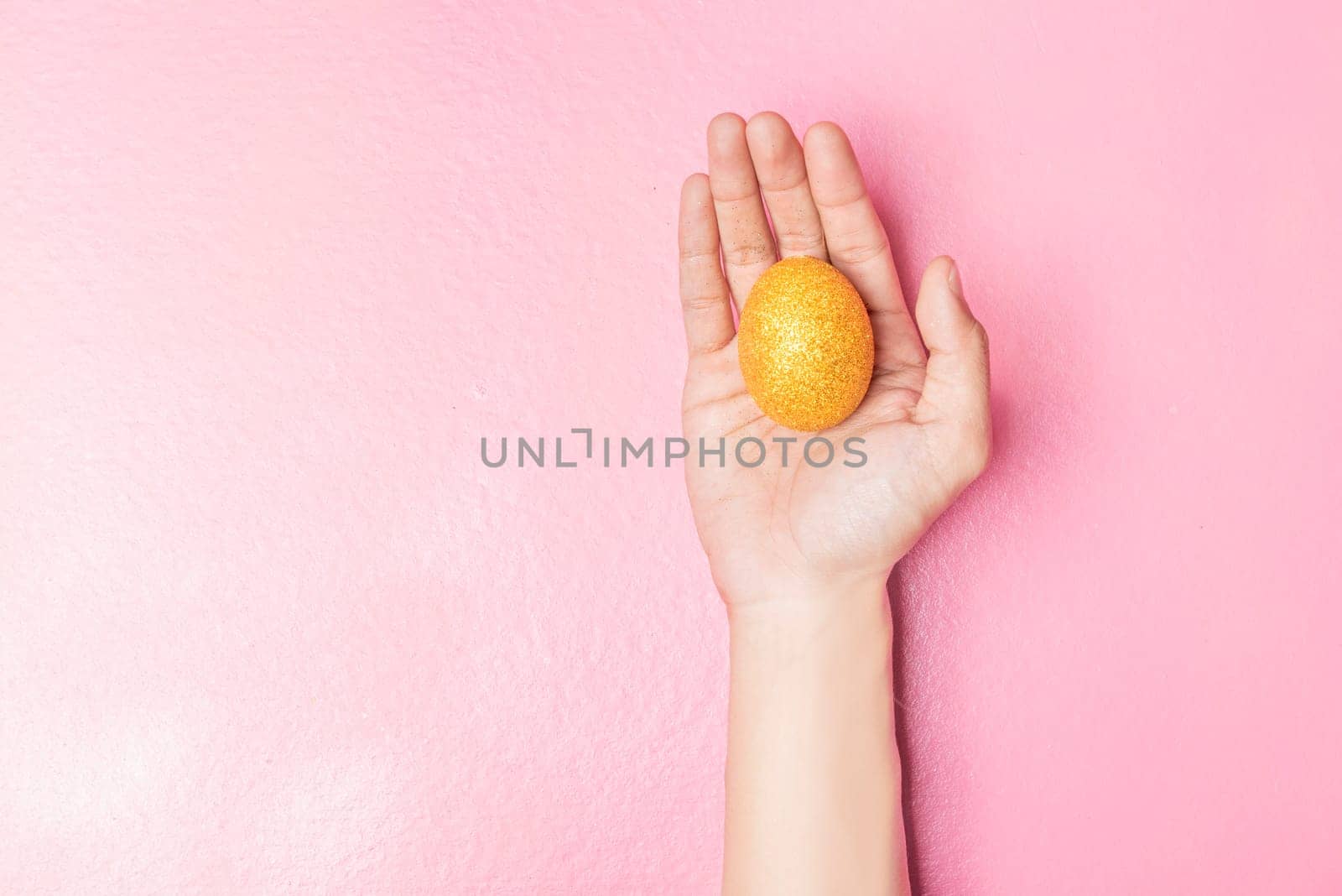 Human hand holding yellow easter egg on pink color background. Happy Easter