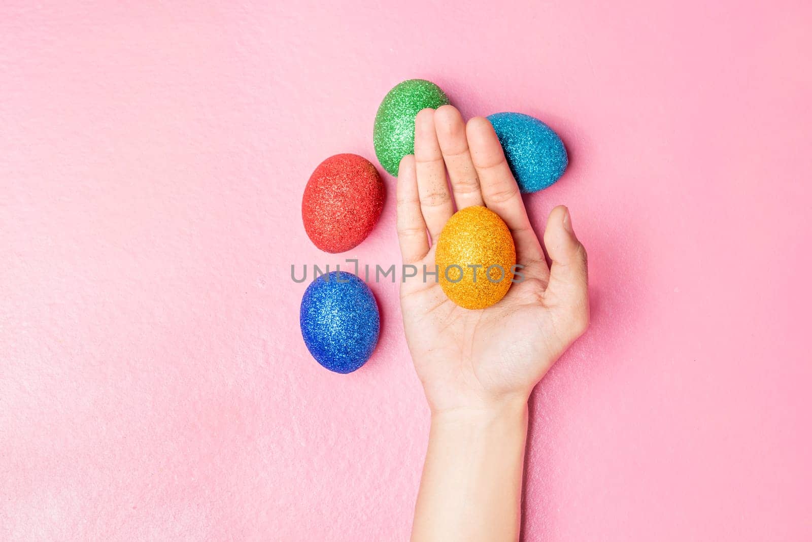 Human hand holding yellow easter egg and colorful easter eggs on pink color background. Happy Easter