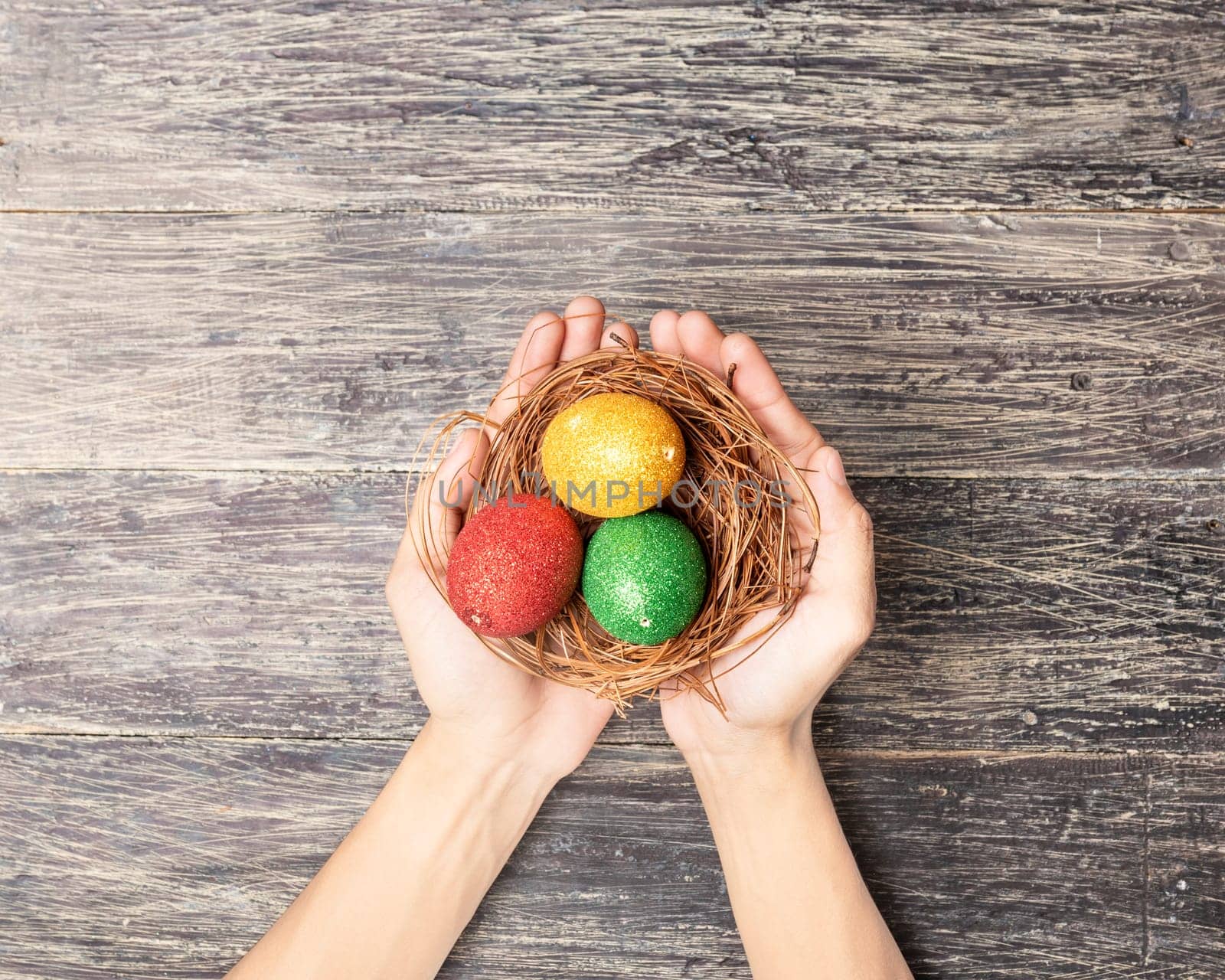 Human hands holding the nest with colorful easter eggs over wooden table background. Happy Easter
