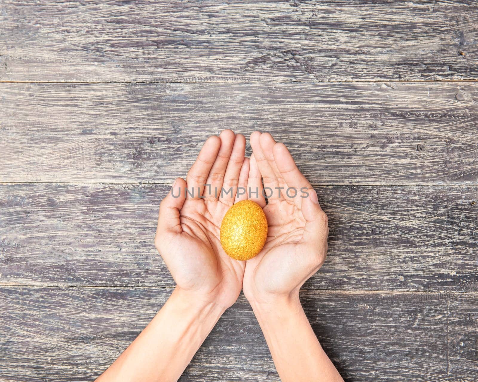 Human hands holding yellow easter egg over wooden table background. Happy Easter