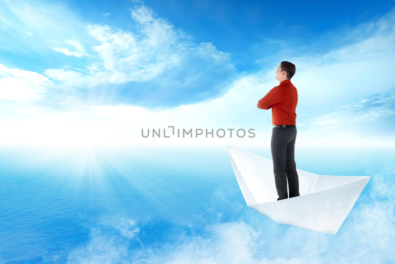 Handsome asian businessman standing on paper boat sailing on blue ocean with blue sky and sunlight background. Business concept