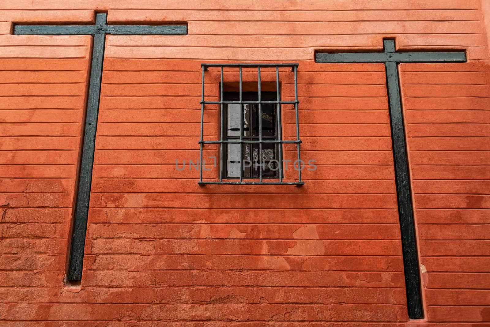 Two crosses on a red wall with a barred window in Seville, Spain