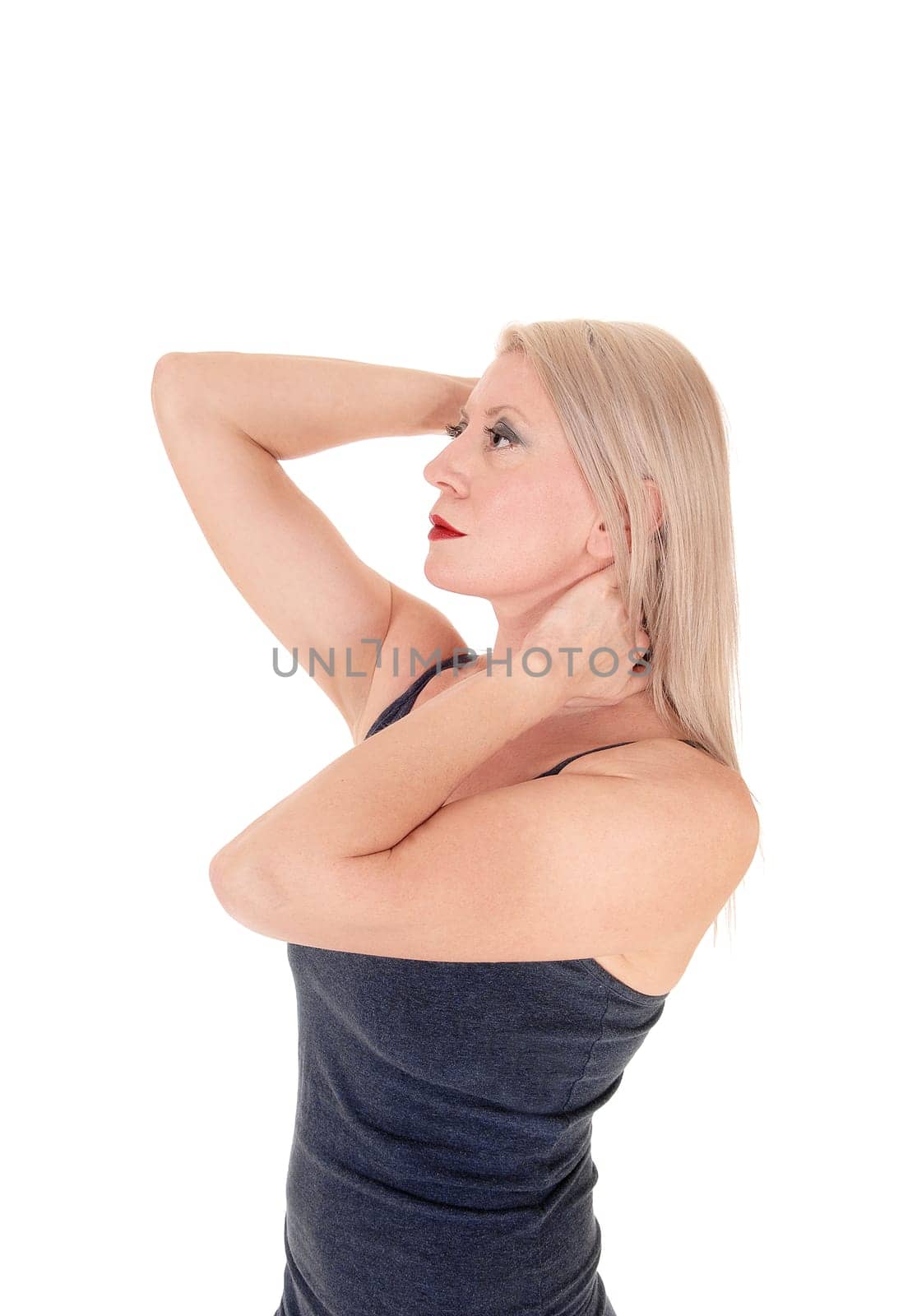 A lovely blond middle age woman standing in a blue dress in profile.with her hands on her head, isolated for white background.