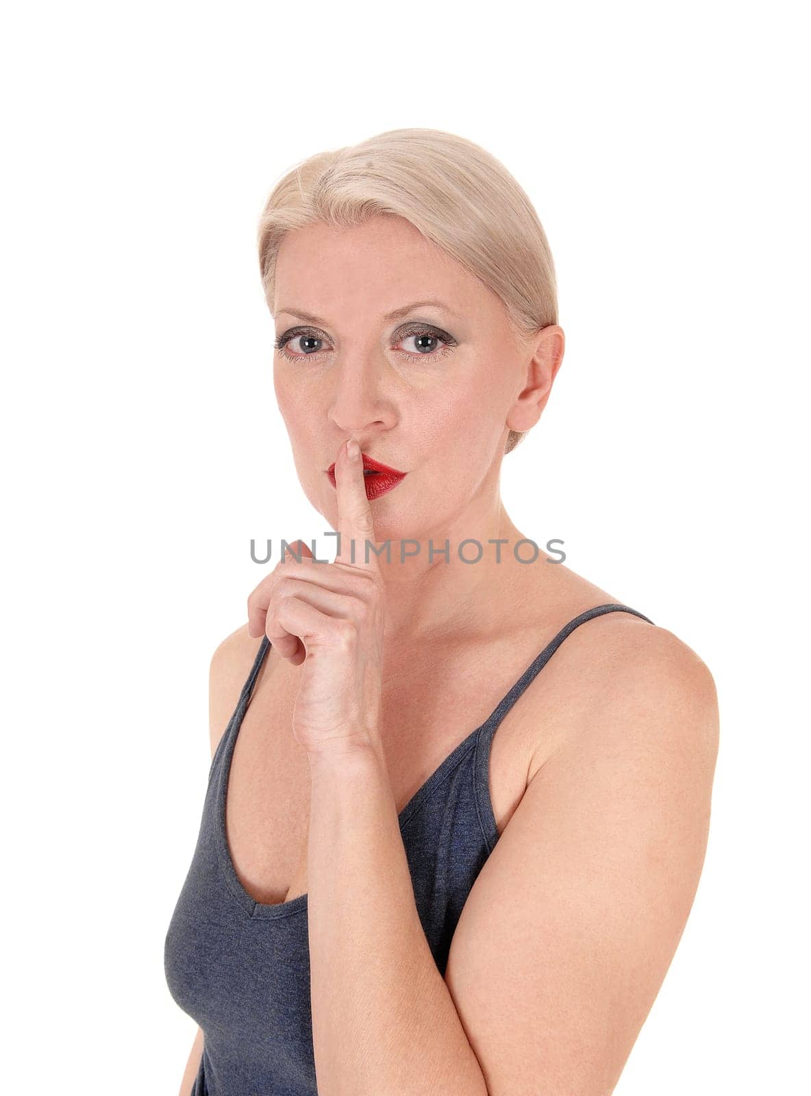 A beautiful middle age blond woman standing in a blue dress with one .finger over her mouth, silence, isolated for white background.