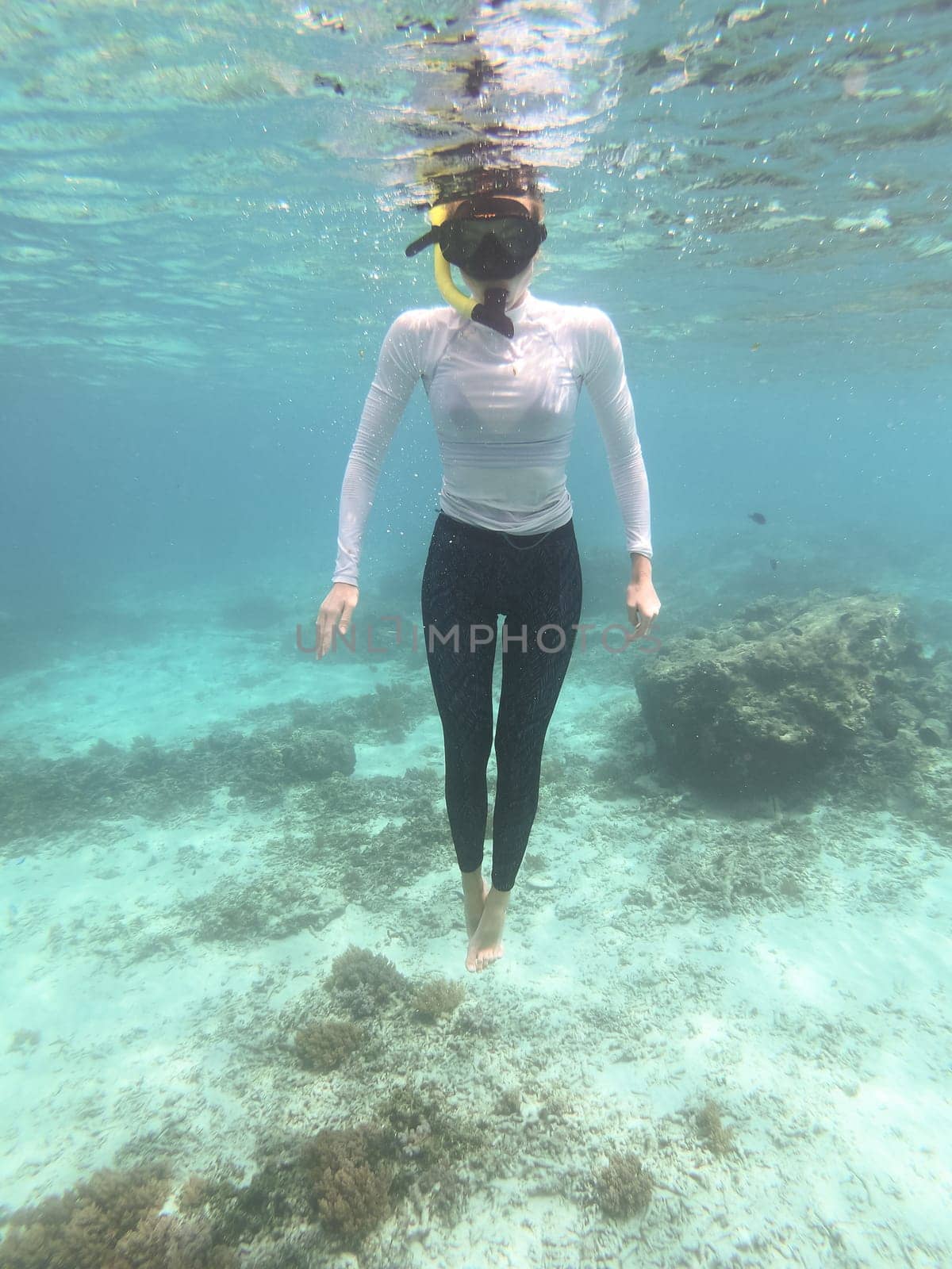 Woman wearing sun protection clothes and snorkeling mask floating in blue sea obove the reef.