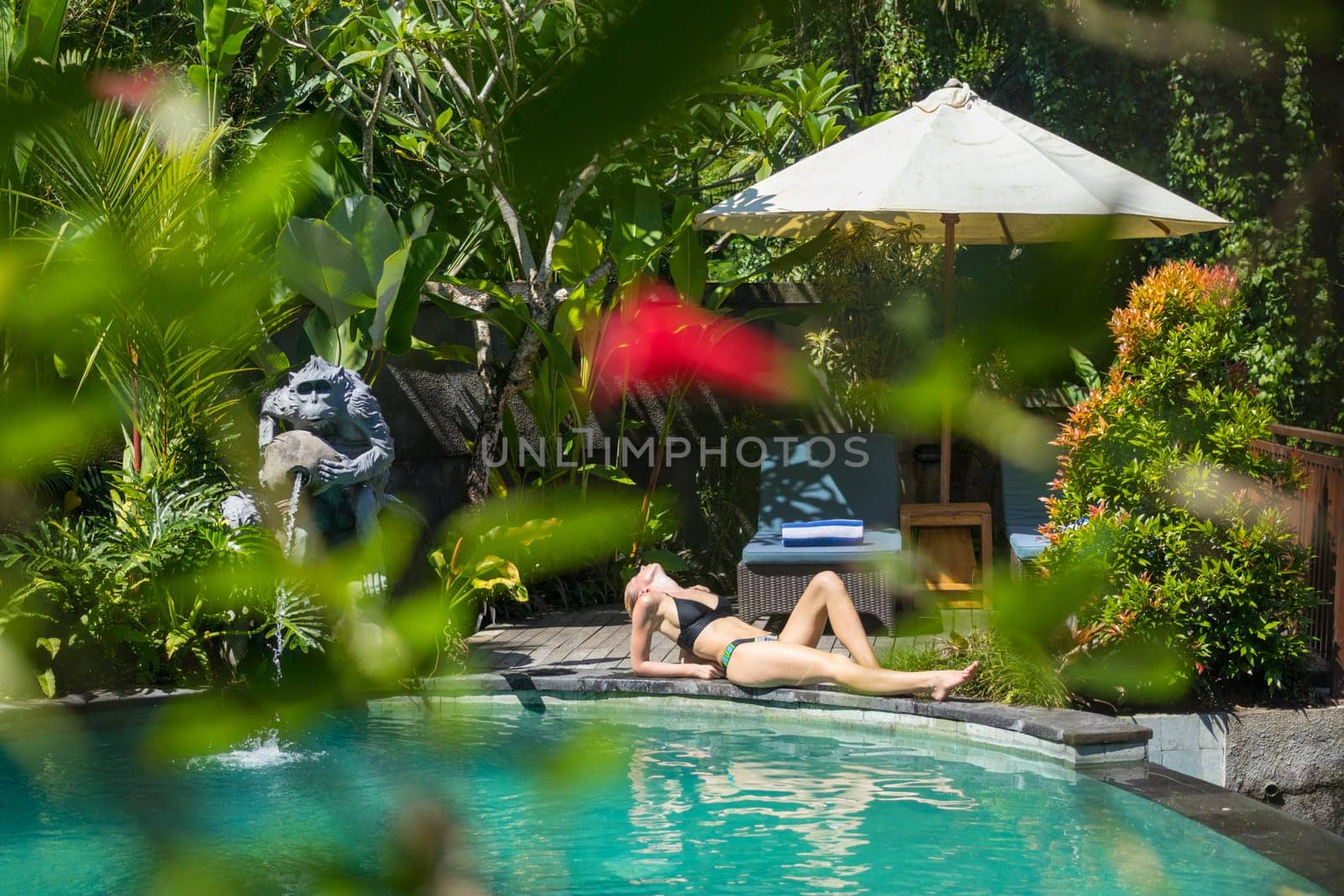 Sensual young woman relaxing in outdoor spa infinity swimming pool surrounded with lush tropical greenery of Ubud, Bali. Wellness, natural beauty and body care concept.