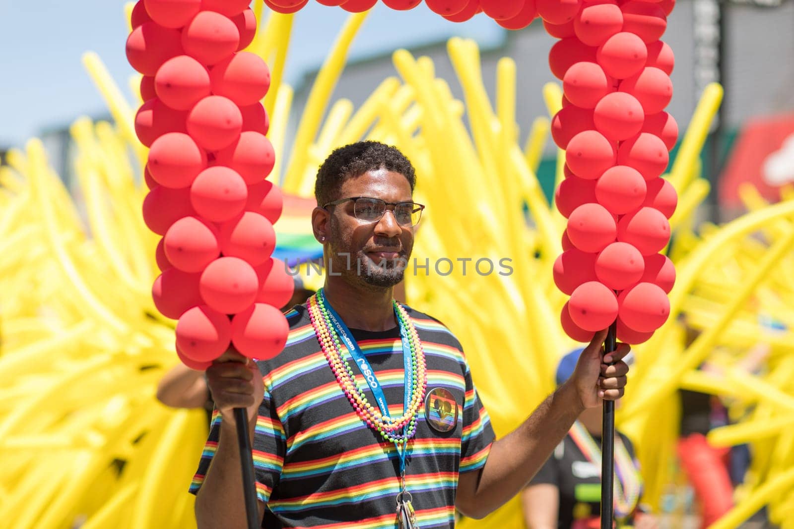 Chicago, Illinois, USA - June 24, 2018 Afro American man holds a letter made of balloons while people wave rainbow flags on the background, celebrating during the LGBTQ Pride Parade in Chicago