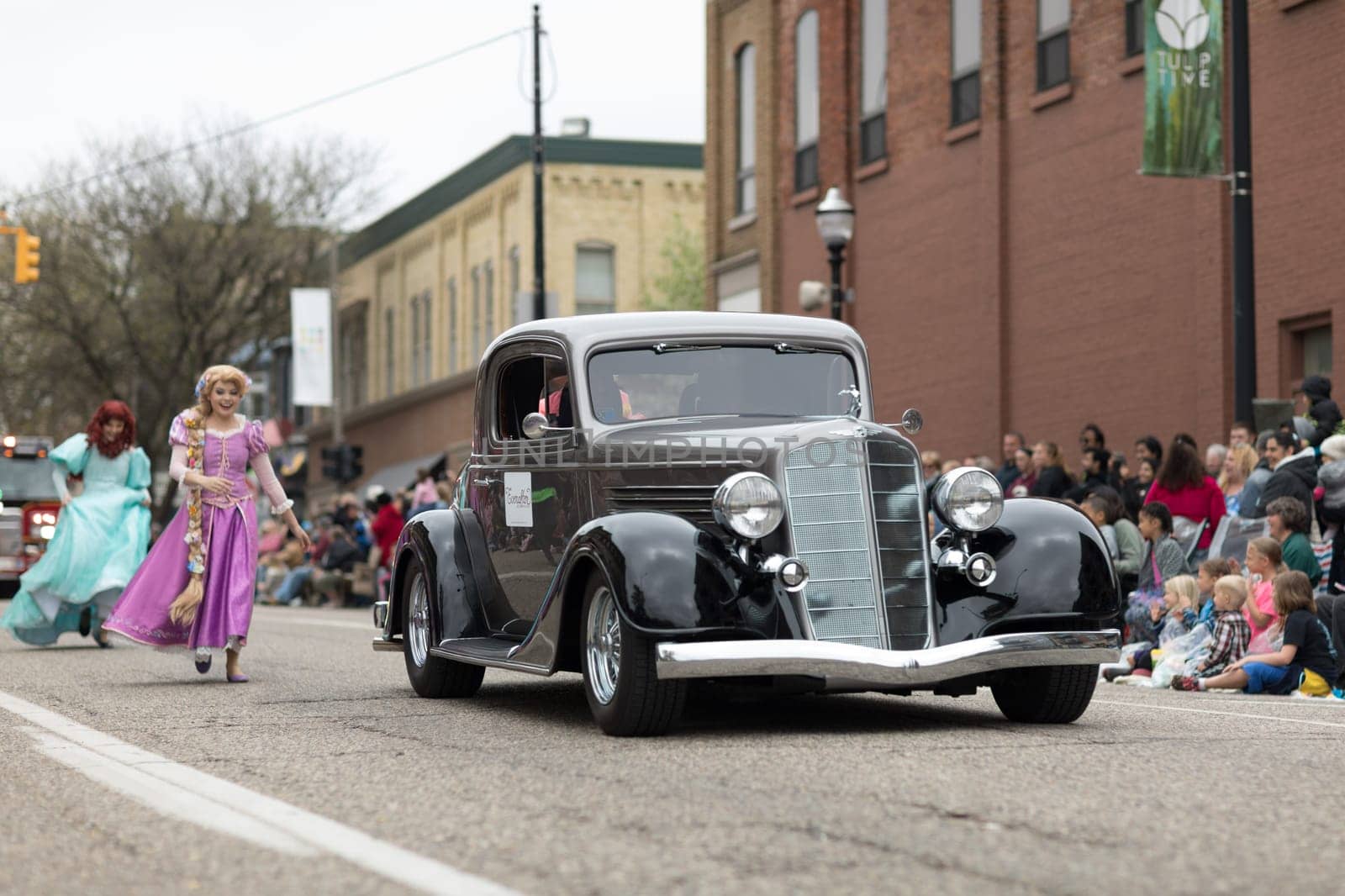 Holland, Michigan, USA - May 12, 2018 Members of Everafter West Michigan dress up as disney princess  with a classic car on the foreground, at the Muziek Parade, during the Tulip Time Festival