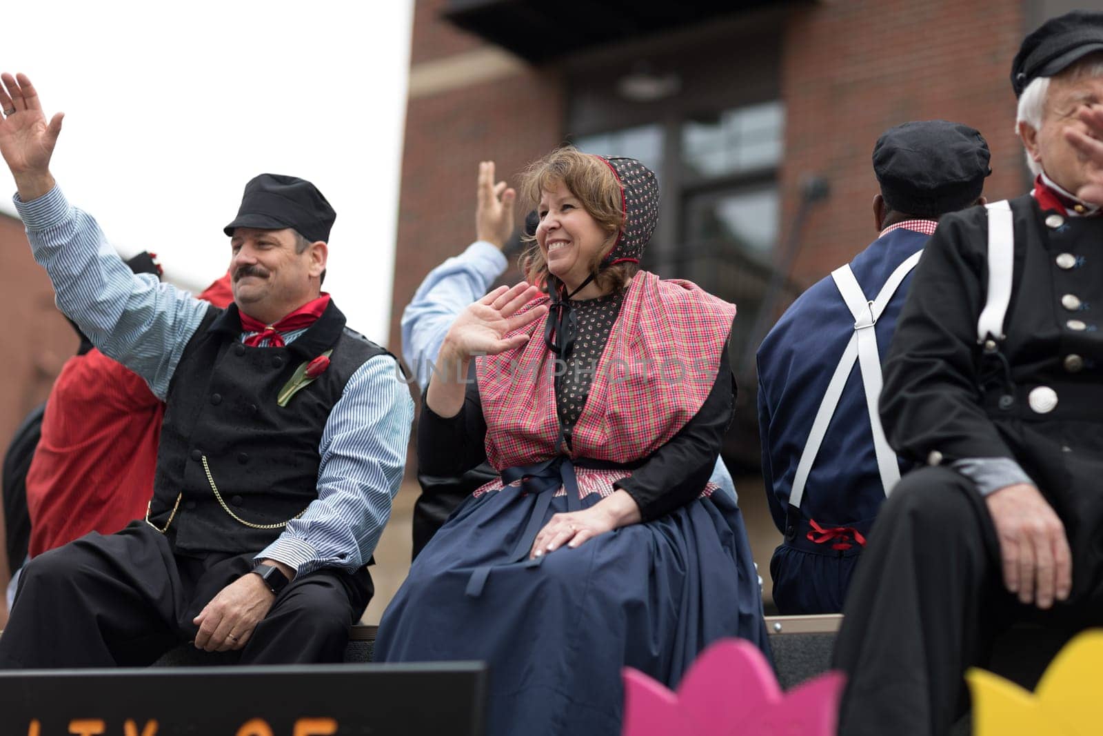 Holland, Michigan, USA - May 12, 2018 Women and men wearing traditional dutch clothing surrounded by tulip flowers, wave at the public, at the Muziek Parade, during the Tulip Time Festival