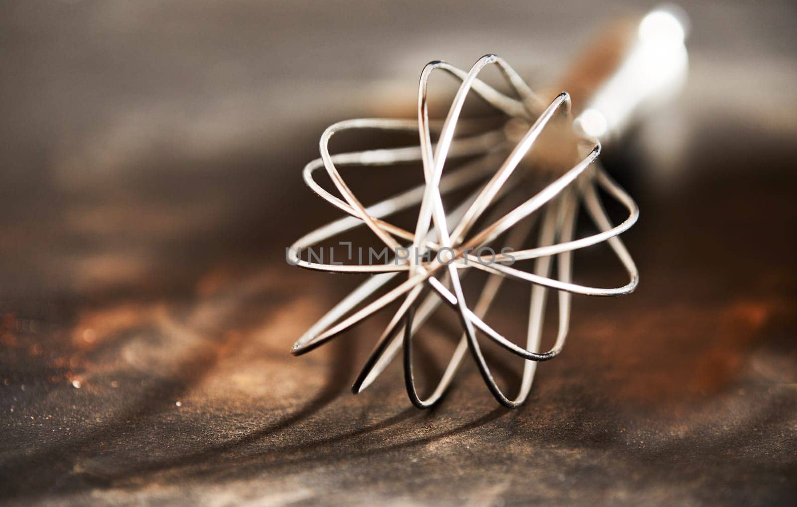 Old vintage steel wire whisk on a rustic wooden kitchen table in a close up view to the end