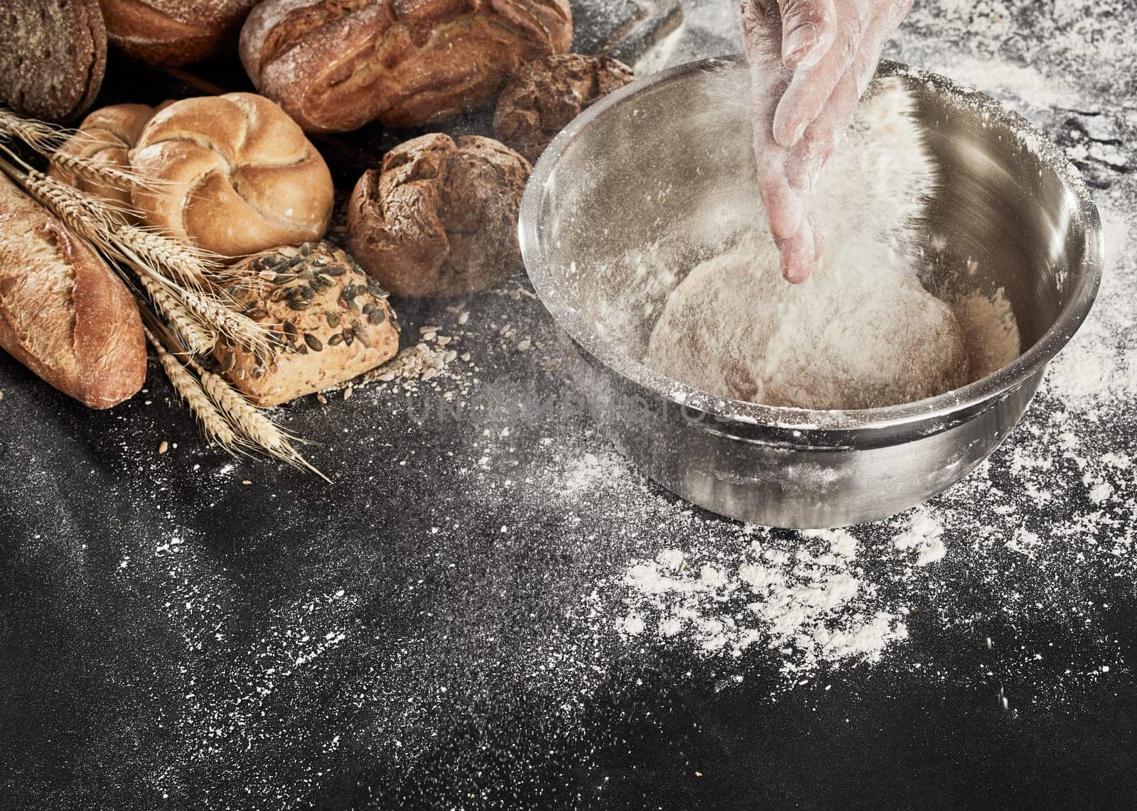 Baker dusting his dough with flour from his hands as he prepares the mixture in a bowl while making an assortment of breads on display
