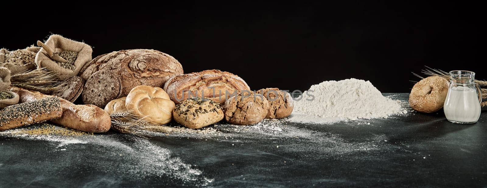 Panorama display of gourmet breads with dough, milk and flour ingredients over a floured kitchen table with copy space